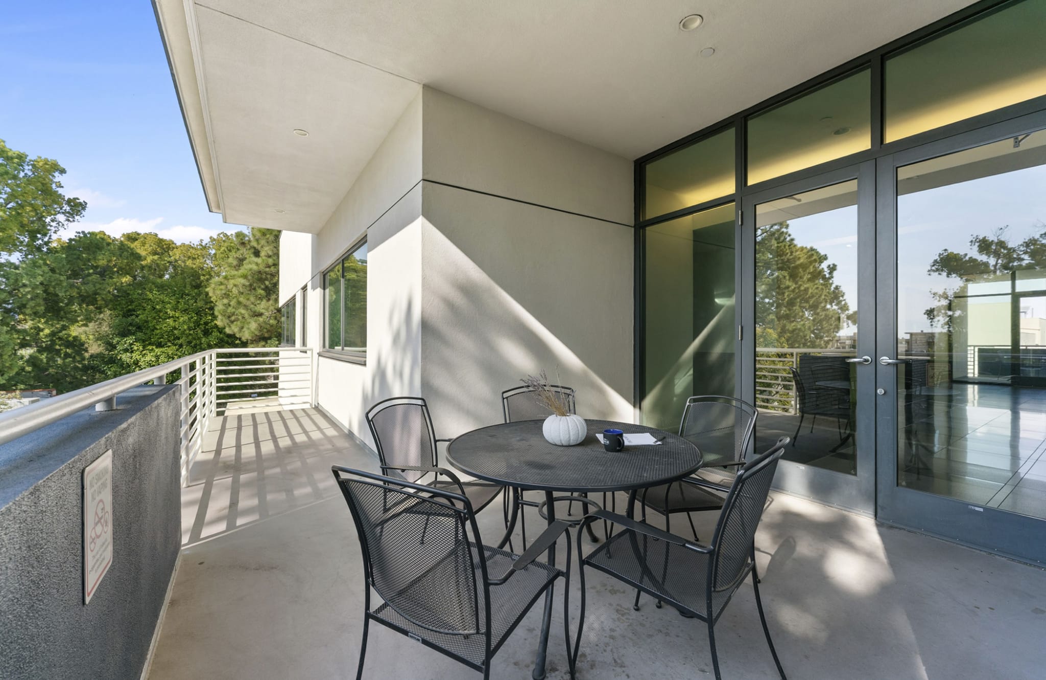 A modern balcony with a round table, four chairs, and a view of trees.