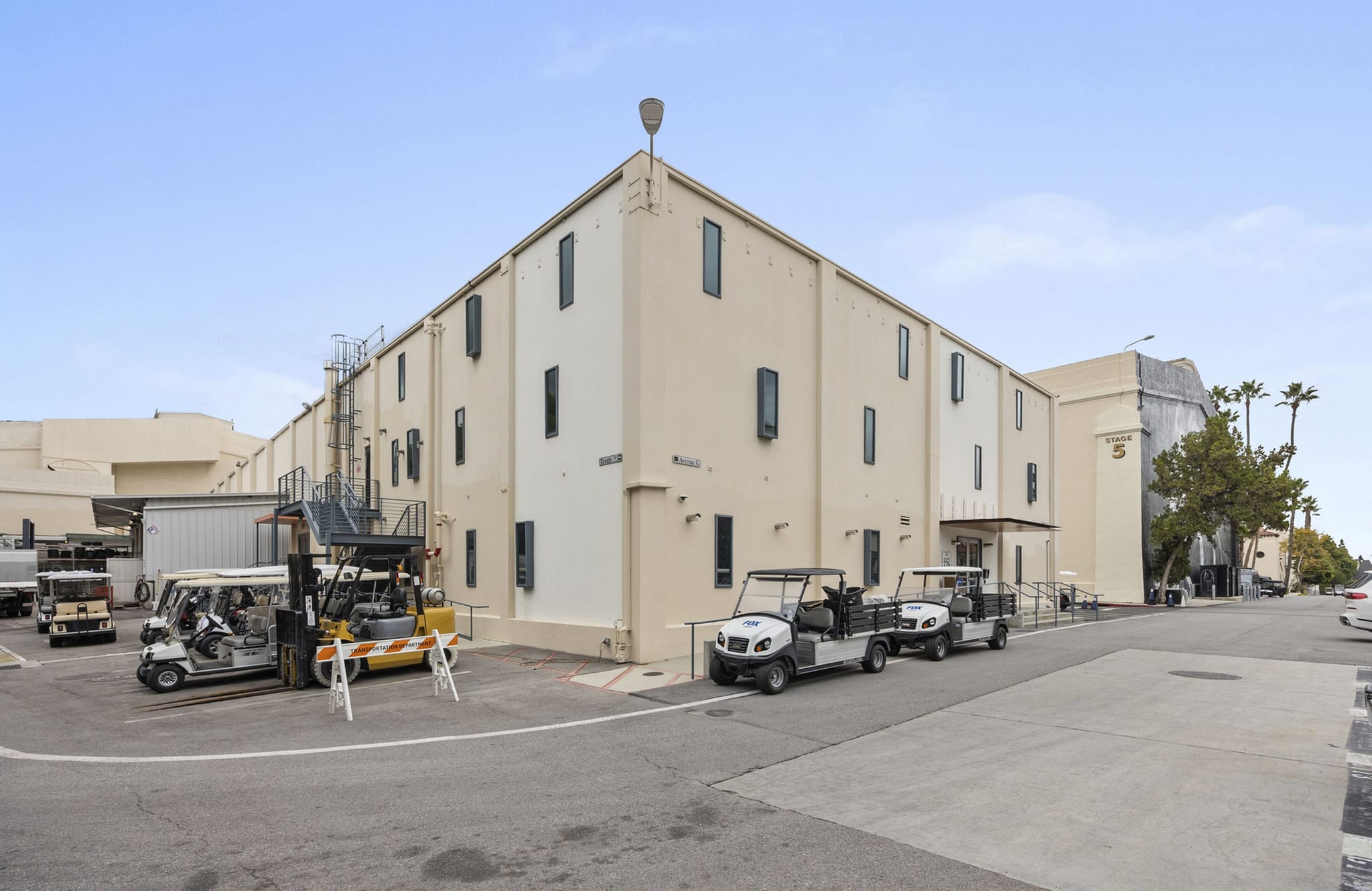 A large cream-colored studio building with several golf carts and a forklift parked outside on an asphalt lot.