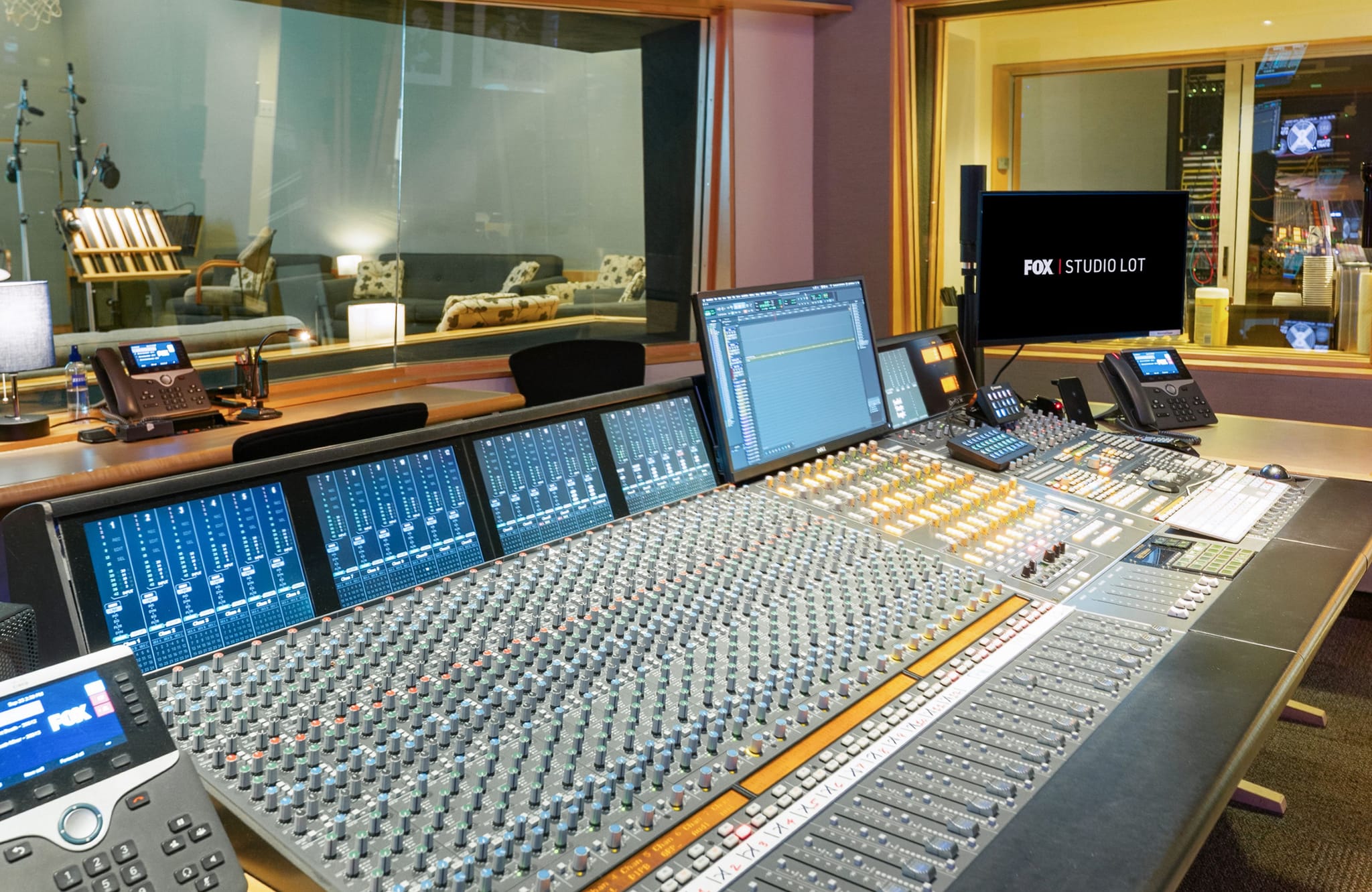 Audio mixing studio control room with a large console and "FOX STUDIO LOT" on a monitor.