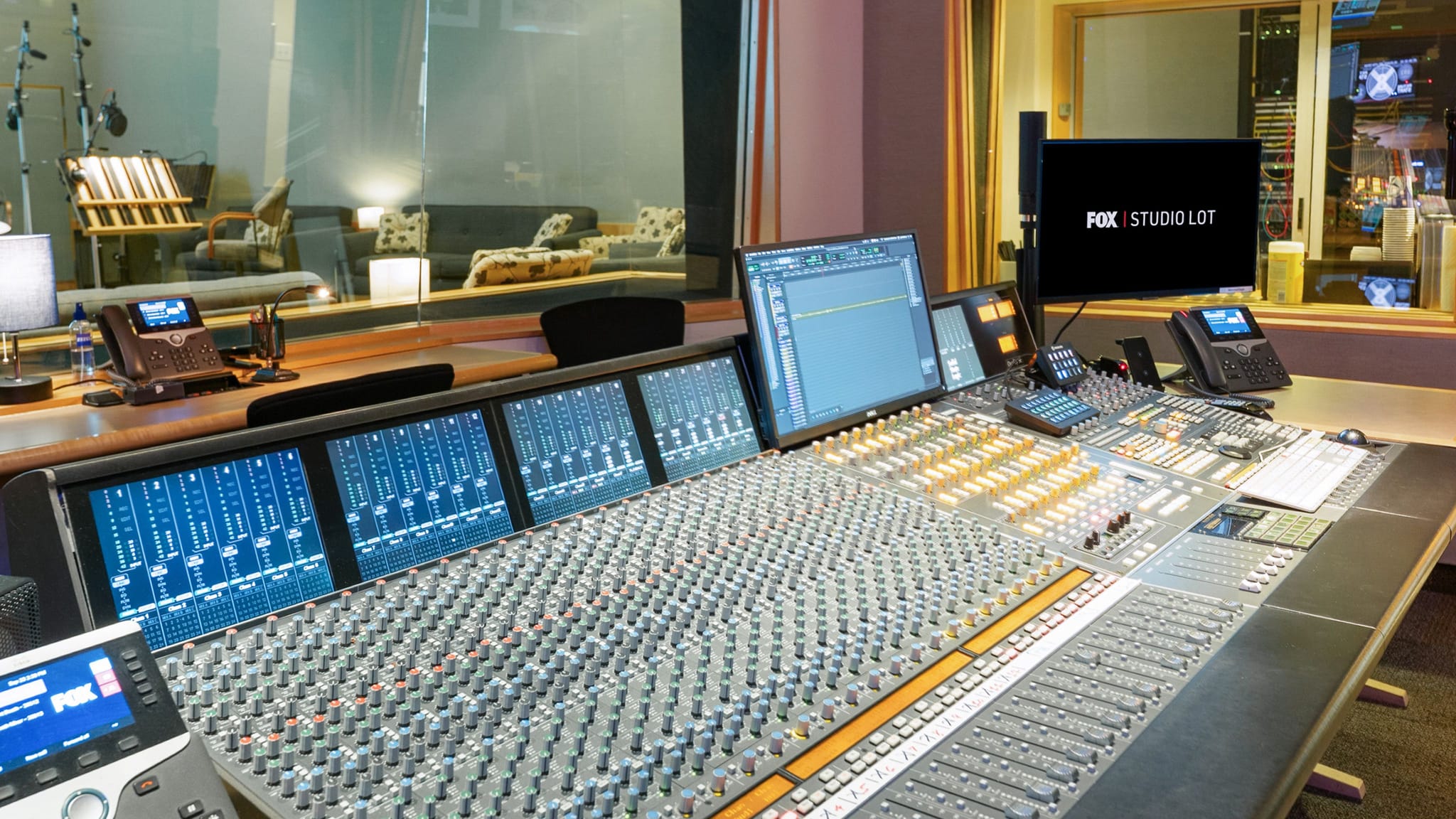 A large professional audio mixing console in a studio, with a monitor displaying "FOX STUDIO LOT".