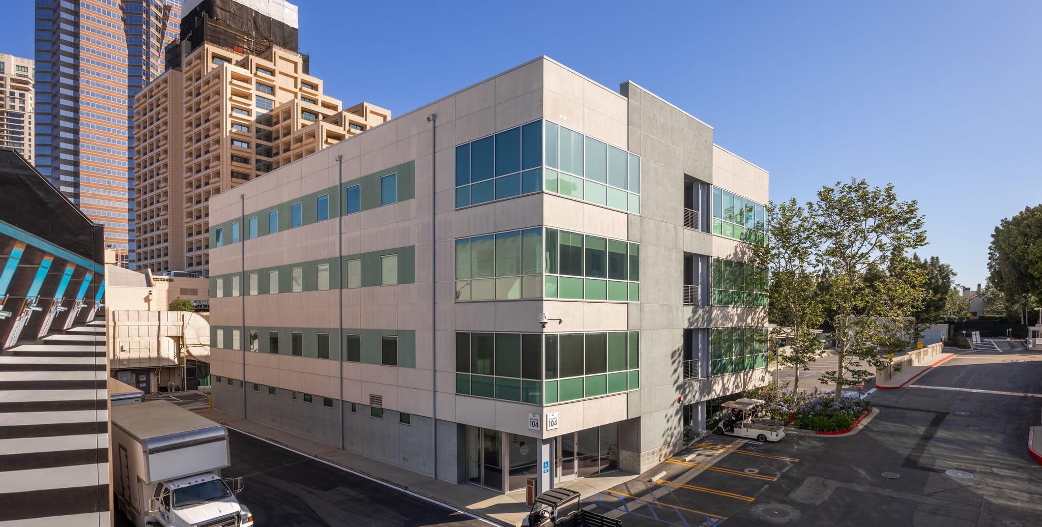 A modern, light-colored, multi-story building with many windows, located on an urban street with a delivery truck.