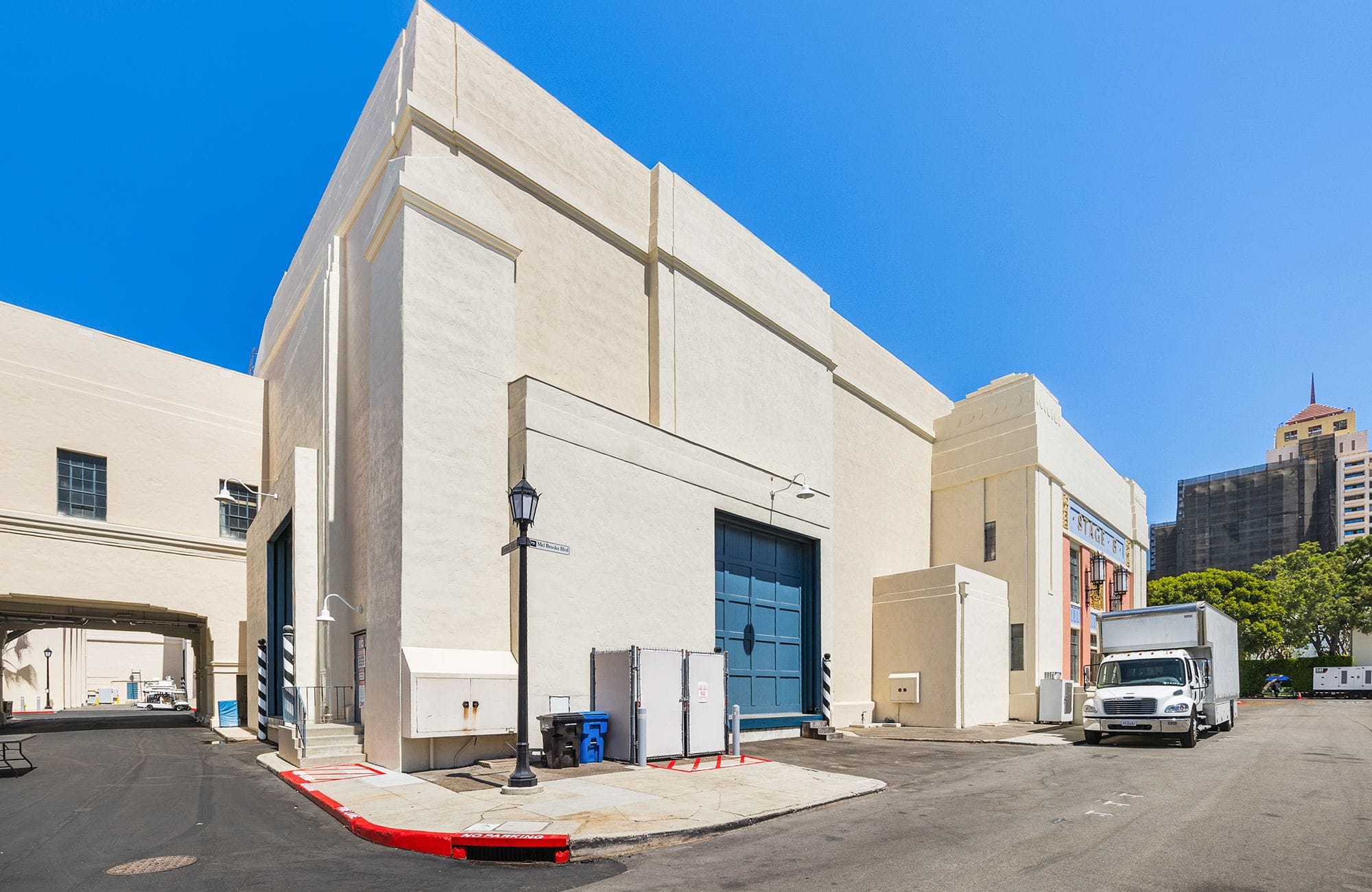 A large cream-colored studio building with blue doors and a white box truck parked outside on a sunny day.