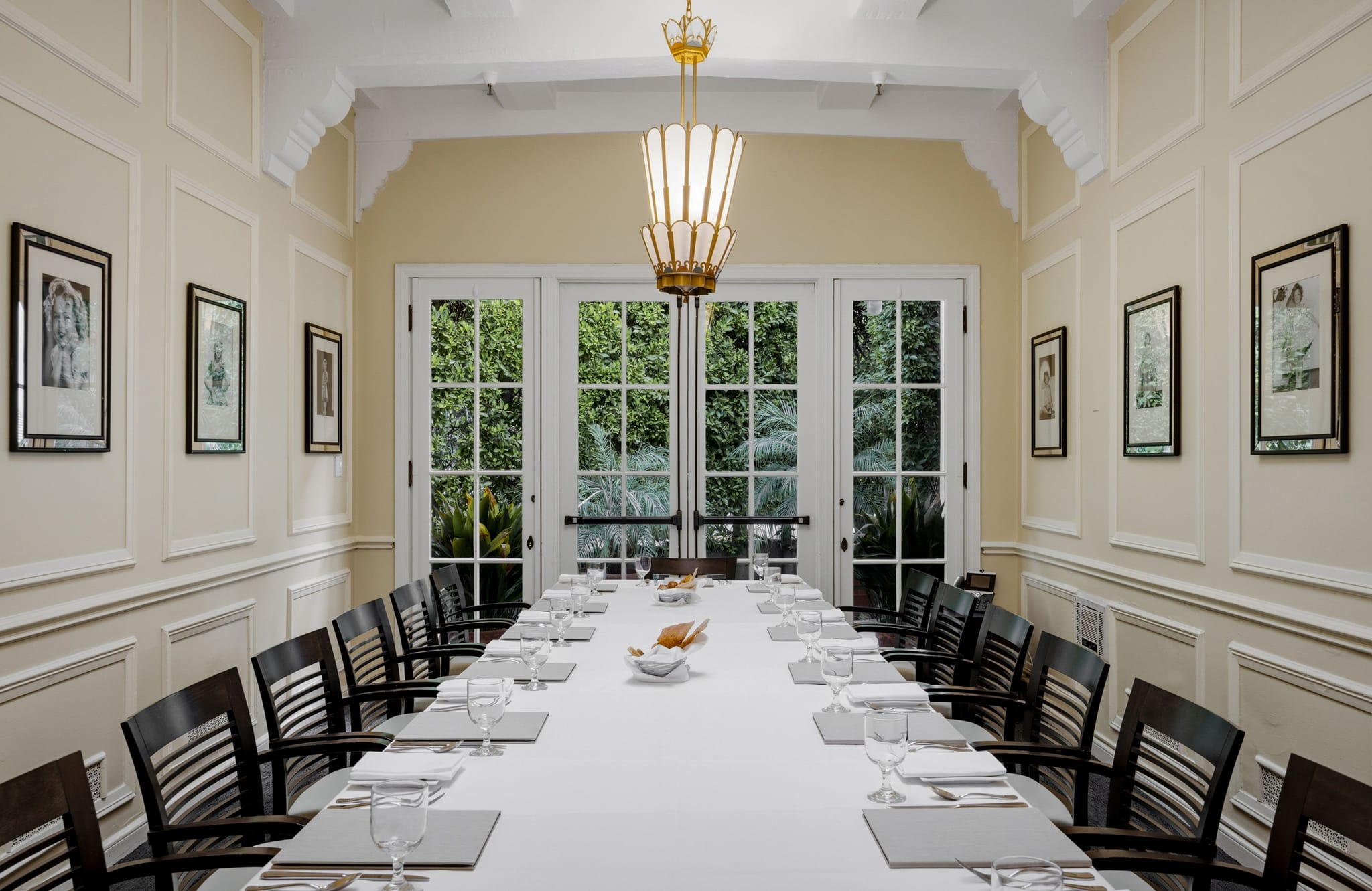 Elegant private dining room with a long, set table, a chandelier, and French doors opening to a lush garden.