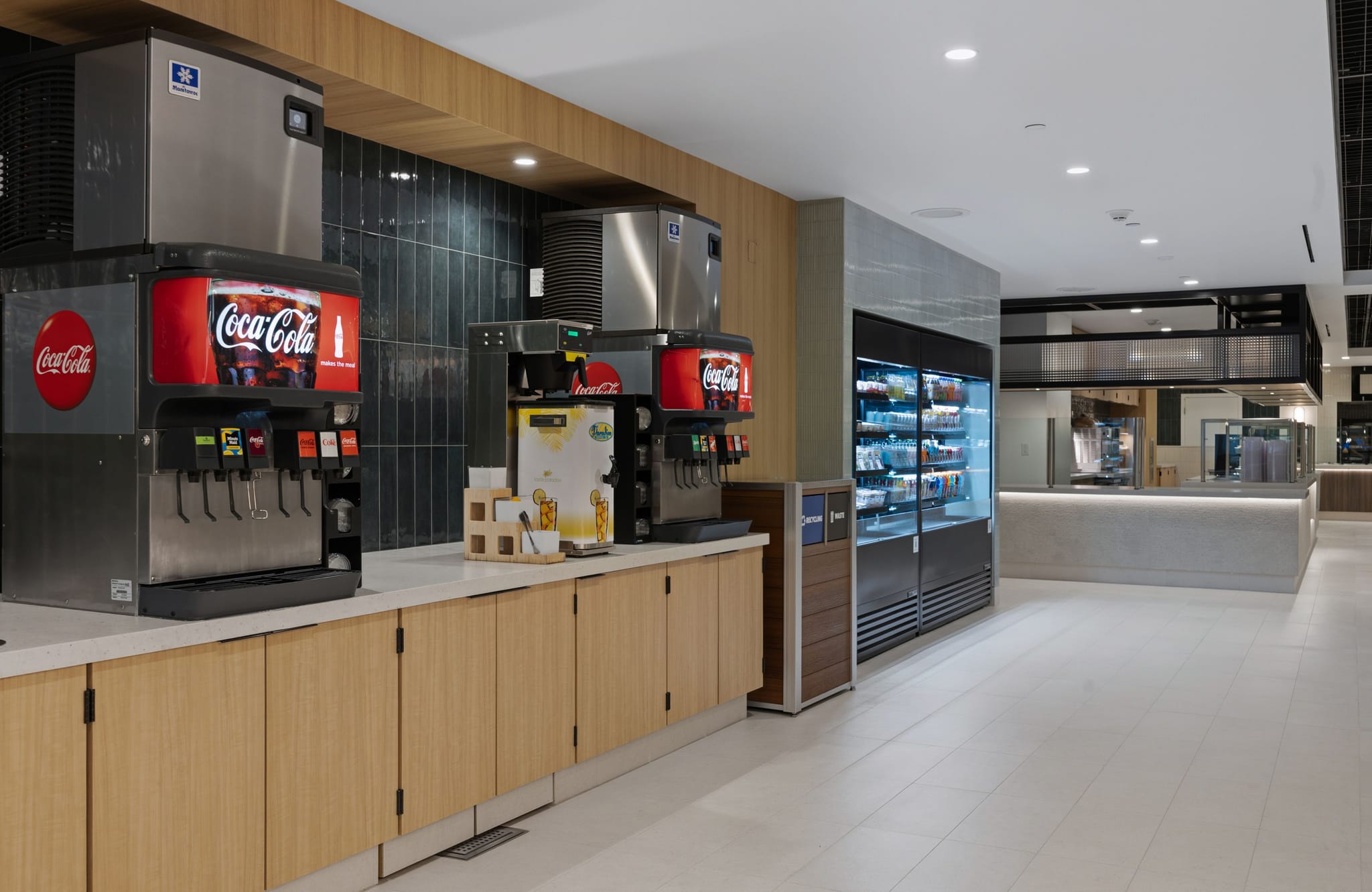 A modern cafeteria with soda fountains, a refrigerated grab-and-go case, and a food serving station.