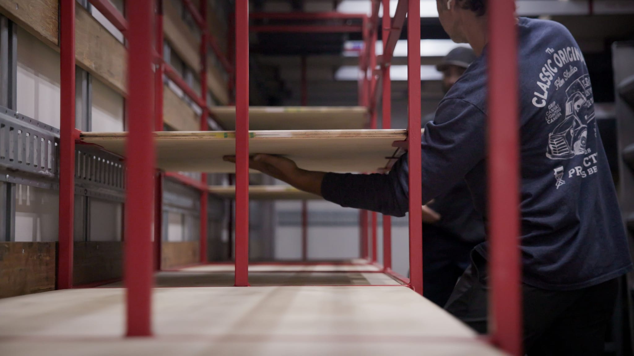 A person installs a wooden shelf into a red metal storage unit.