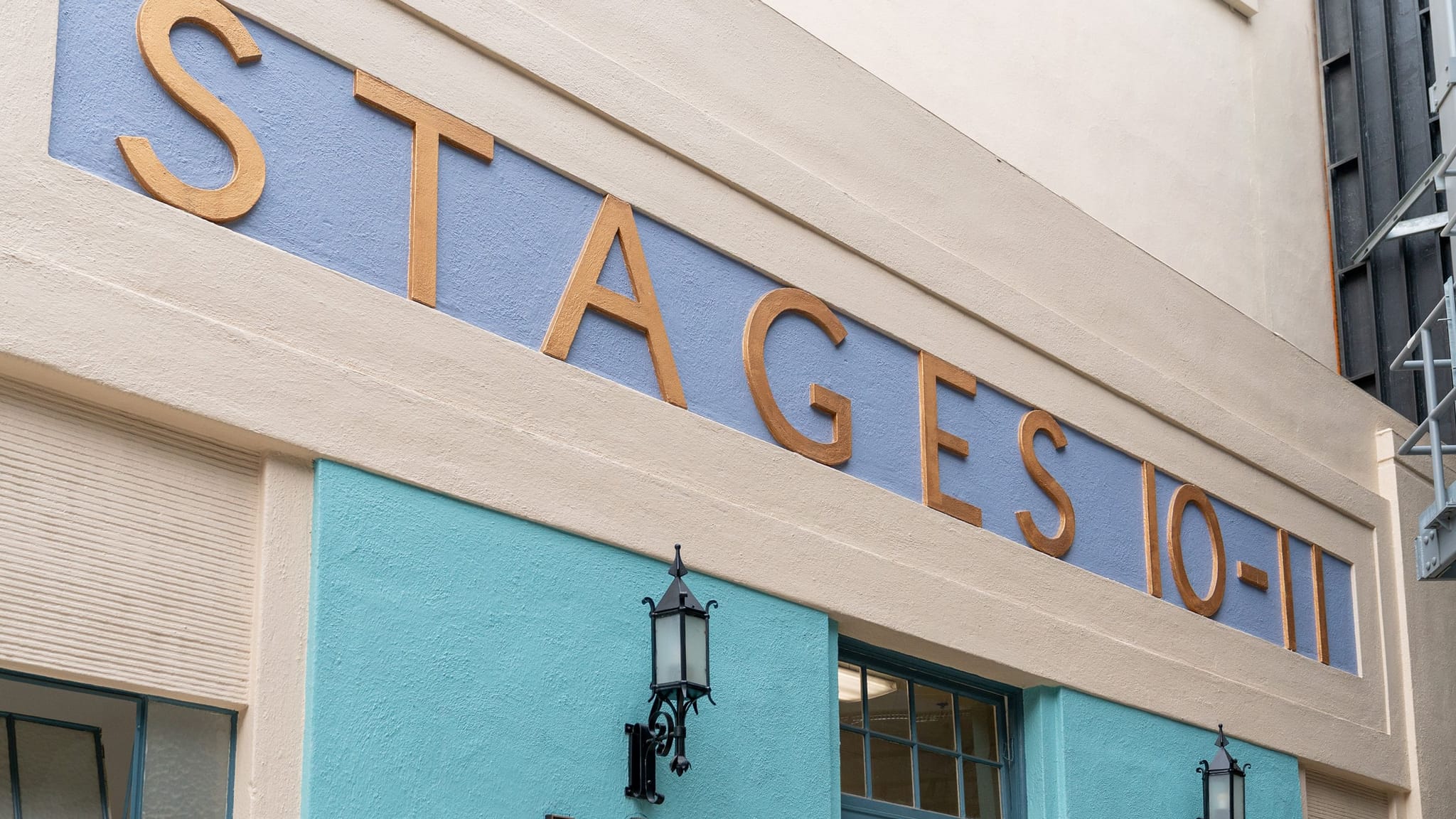 Sign reading "STAGES 10-11" in gold letters on a blue building with cream trim and black lanterns.