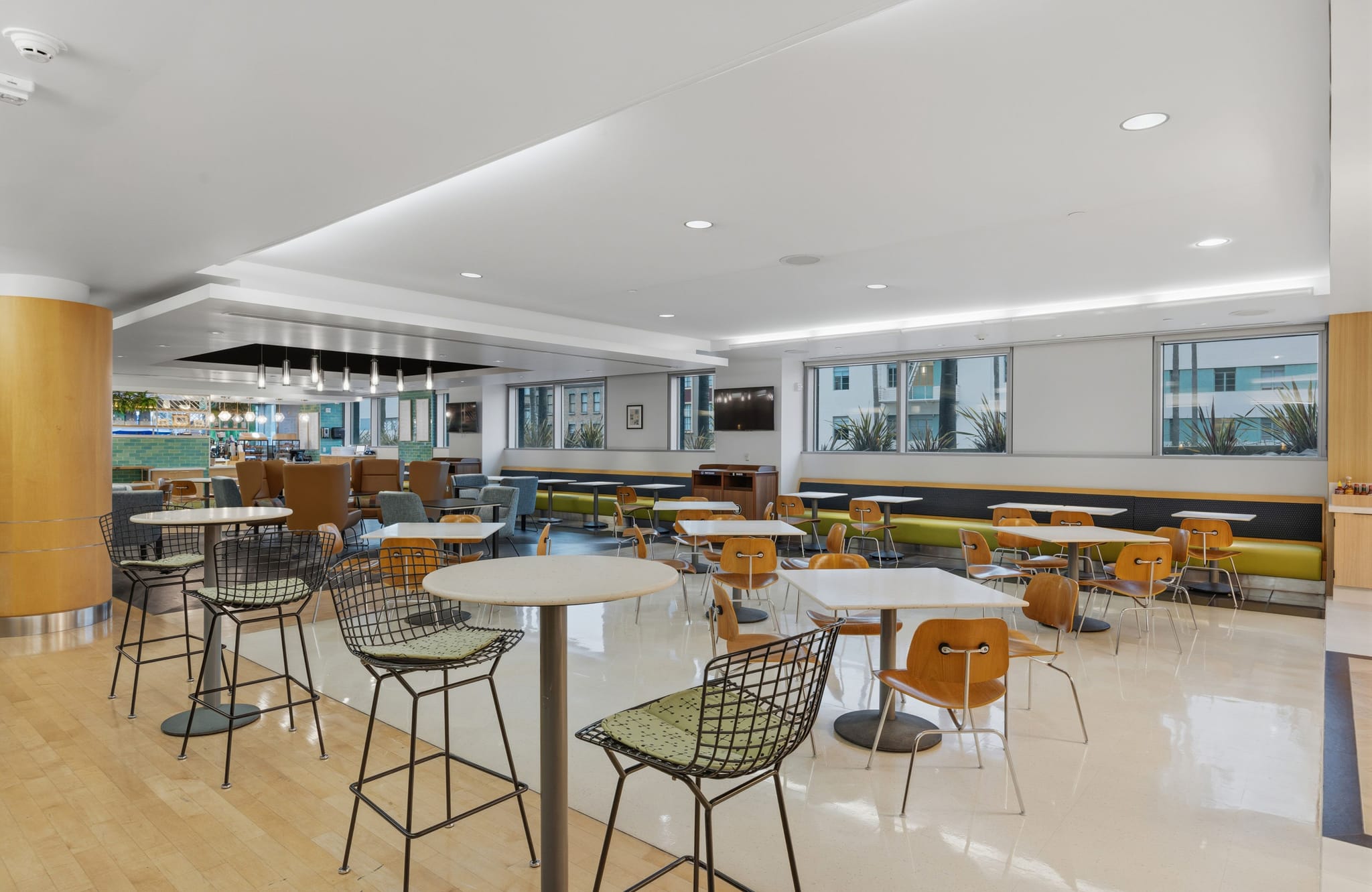 A bright, modern common area with diverse seating including high-top tables, cafe tables, and built-in benches.
