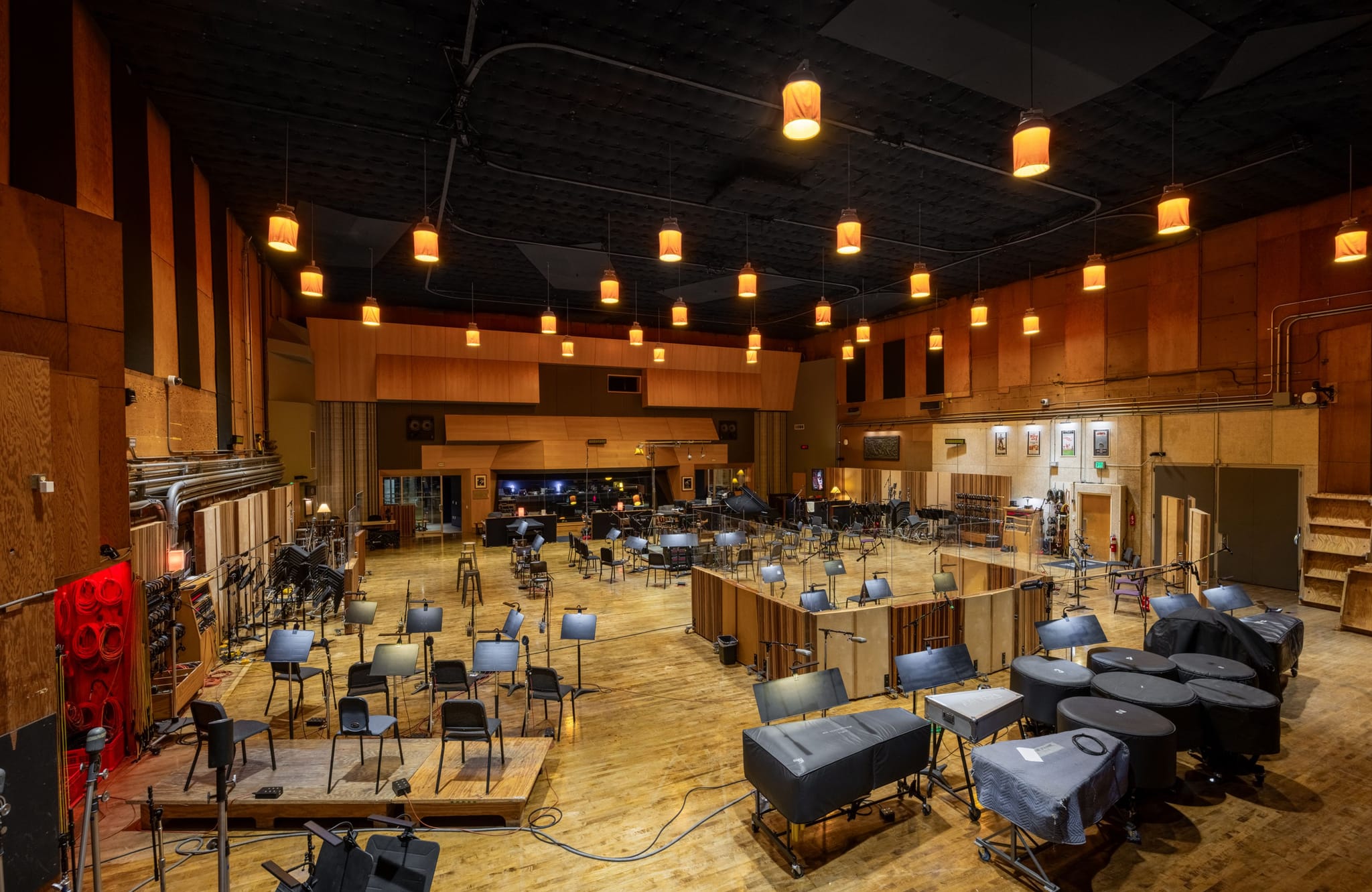 Large, empty orchestral recording studio with chairs, music stands, and covered percussion instruments arranged on a wooden floor.