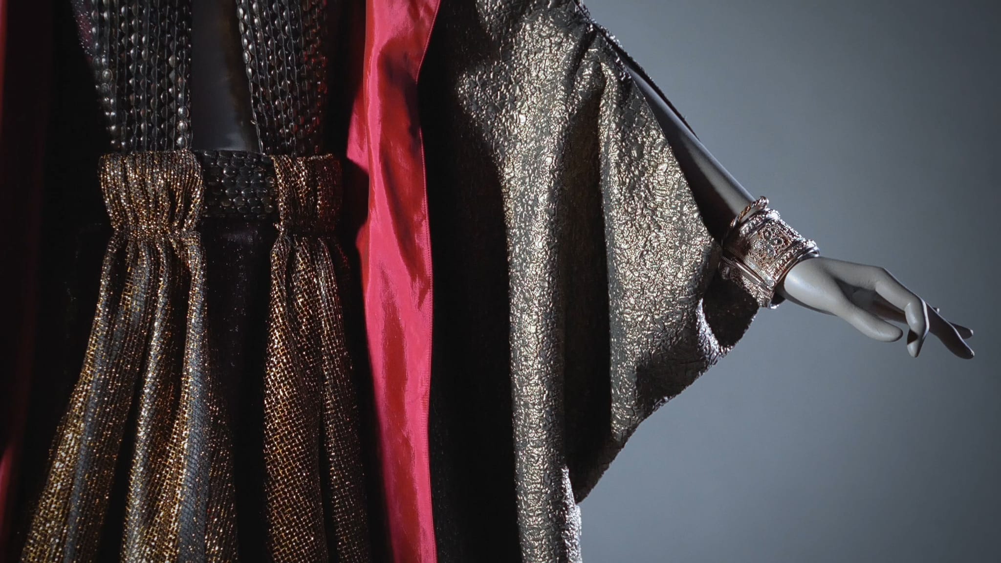 Shimmering dark gold and red dress with an ornate cuff on a mannequin.
