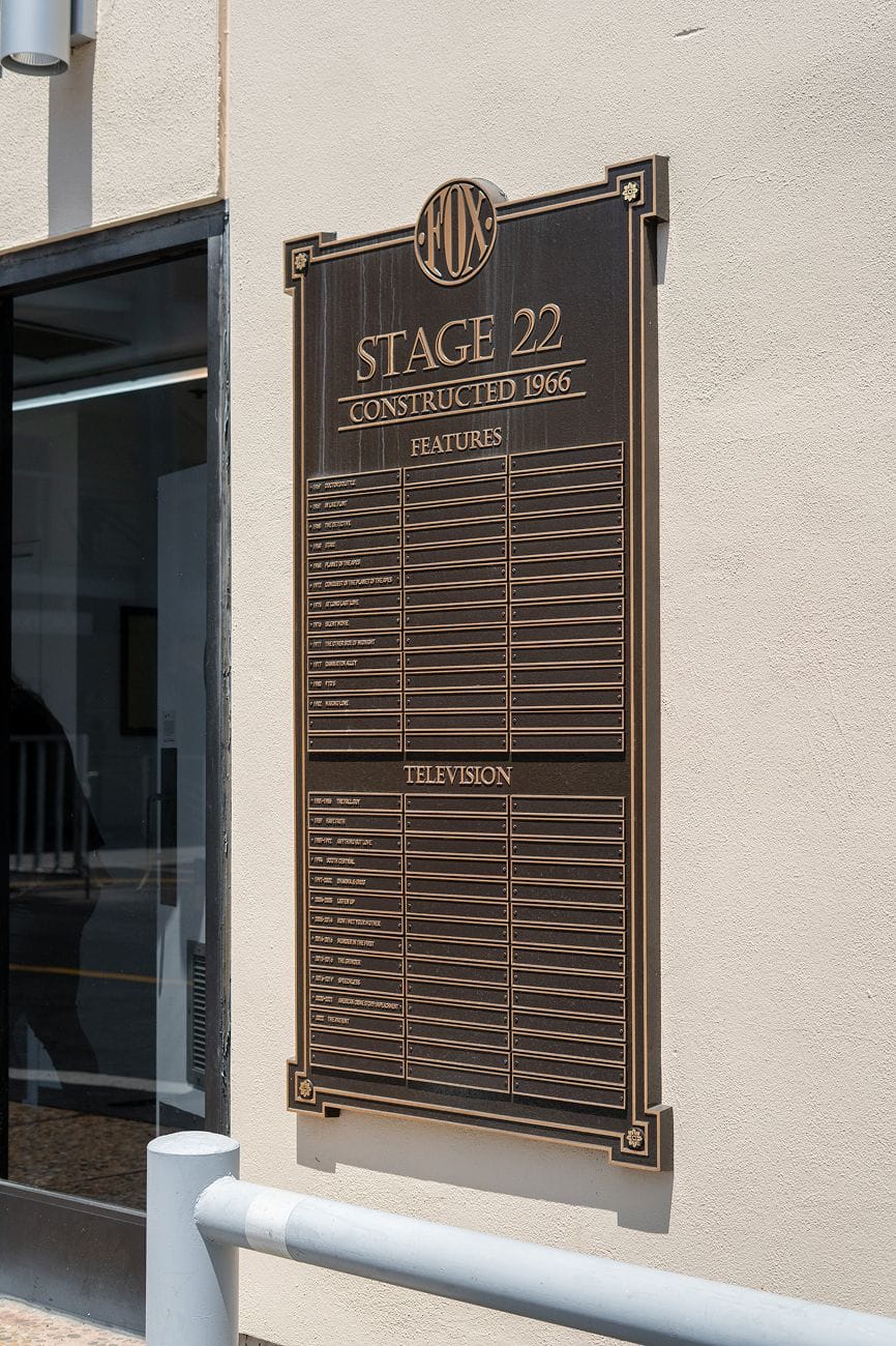 A bronze plaque for FOX Stage 22, constructed 1966, with empty slots for features and television productions, mounted on a wall.