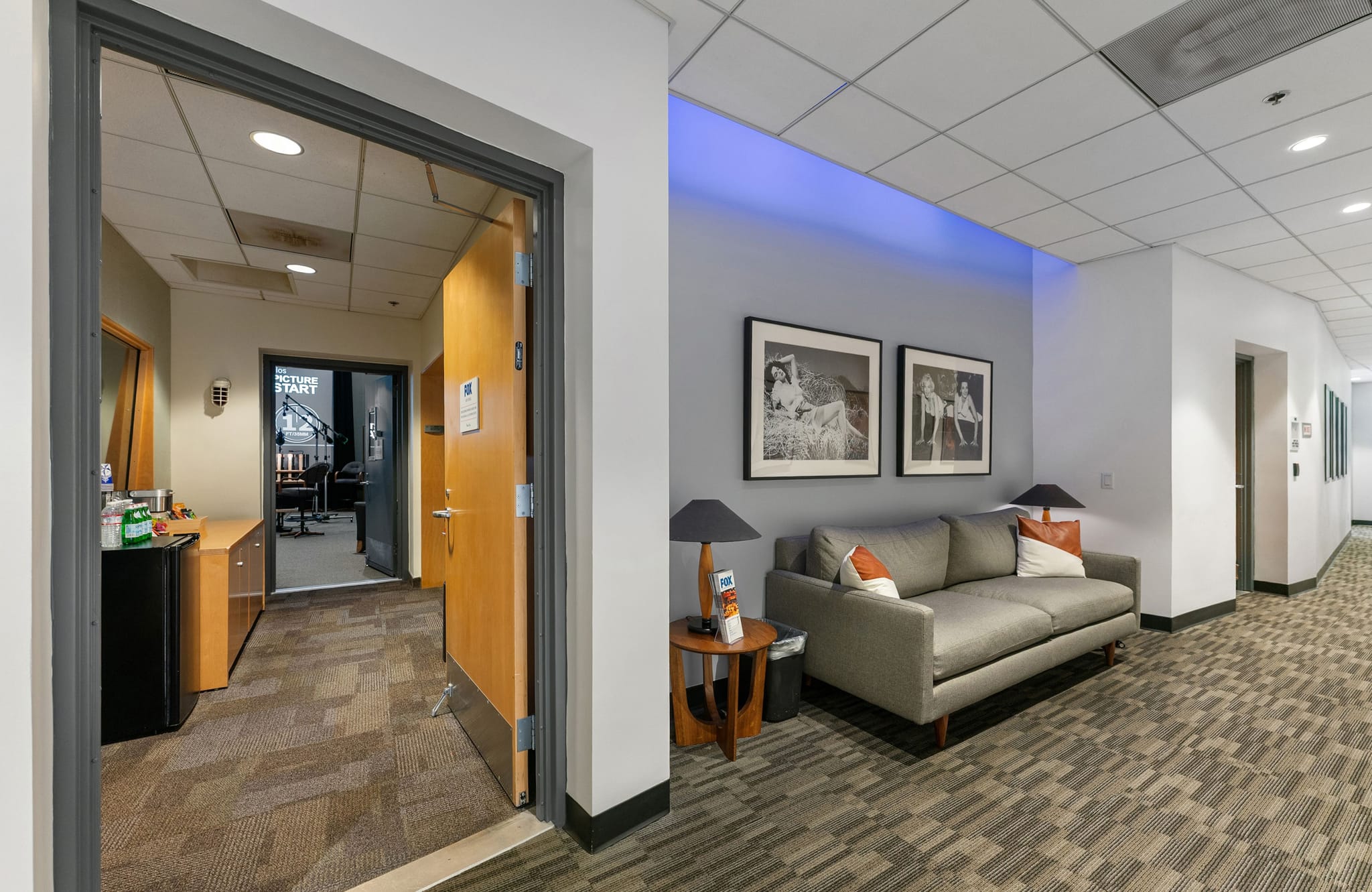A waiting area with a gray sofa, framed art, and an open doorway leading to an office.