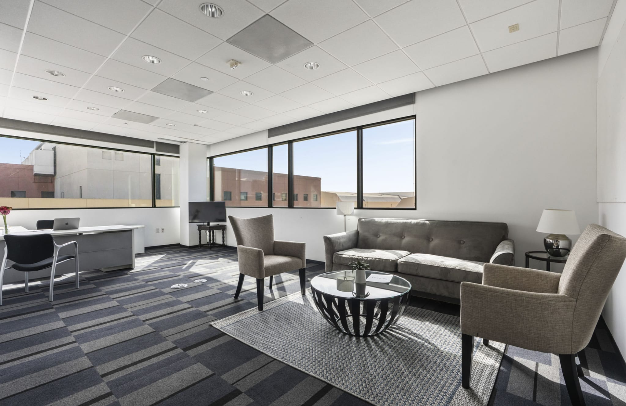 Modern office with a desk, sofa, two armchairs, and large windows.