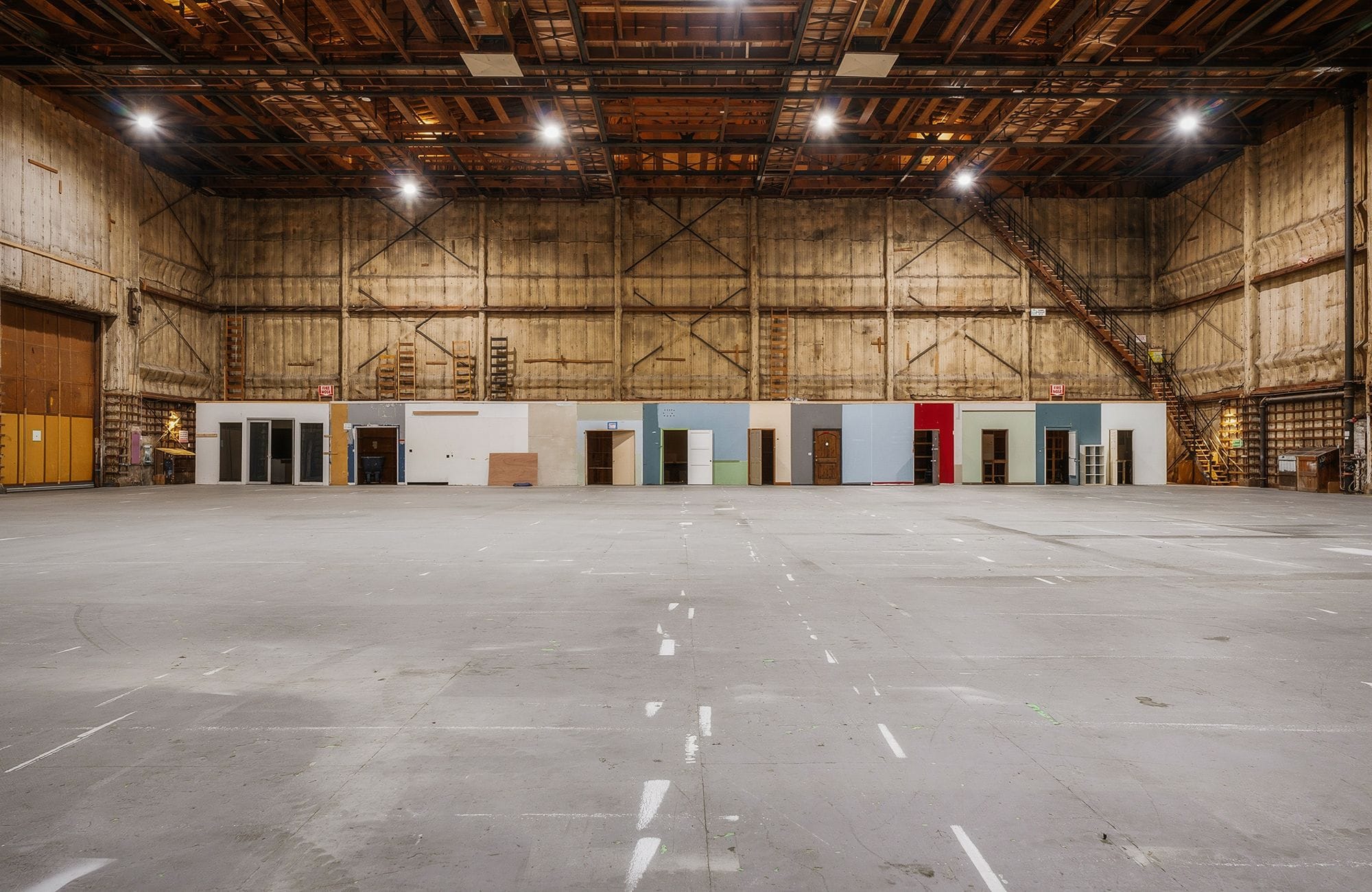 Empty industrial warehouse with a long, low wall of various colored doors and panels across the center.