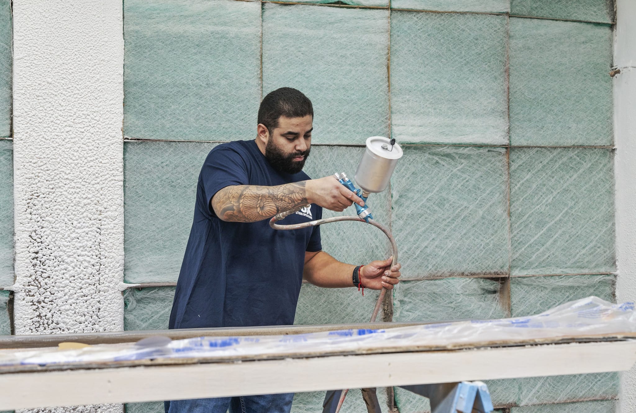 A man spray paints in a workshop against a wall of green air filters.