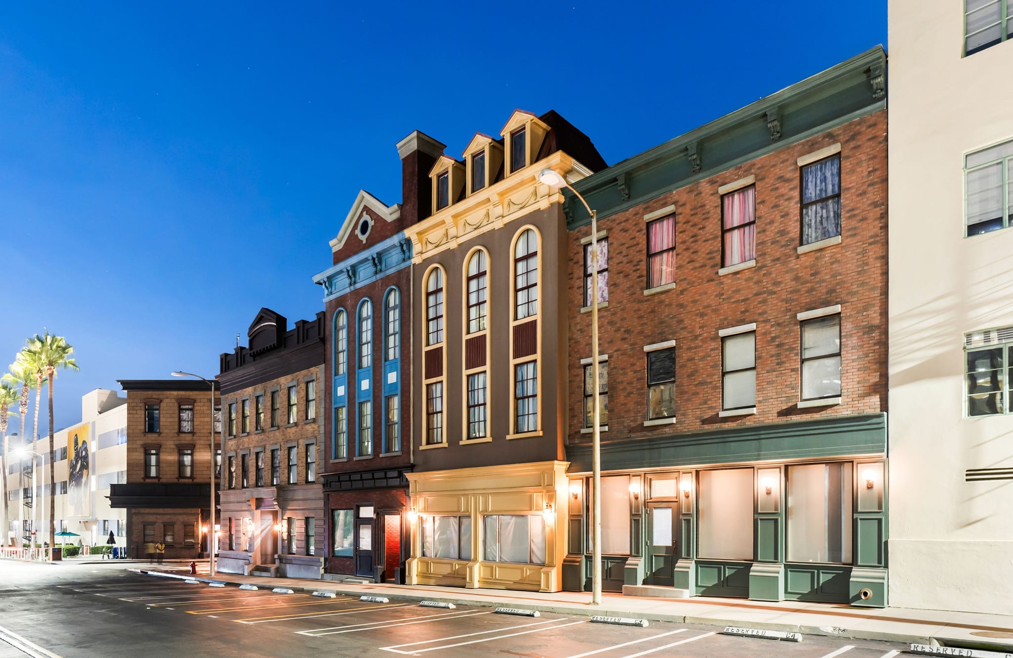 Row of illuminated buildings with diverse facades along a street with parking at night.