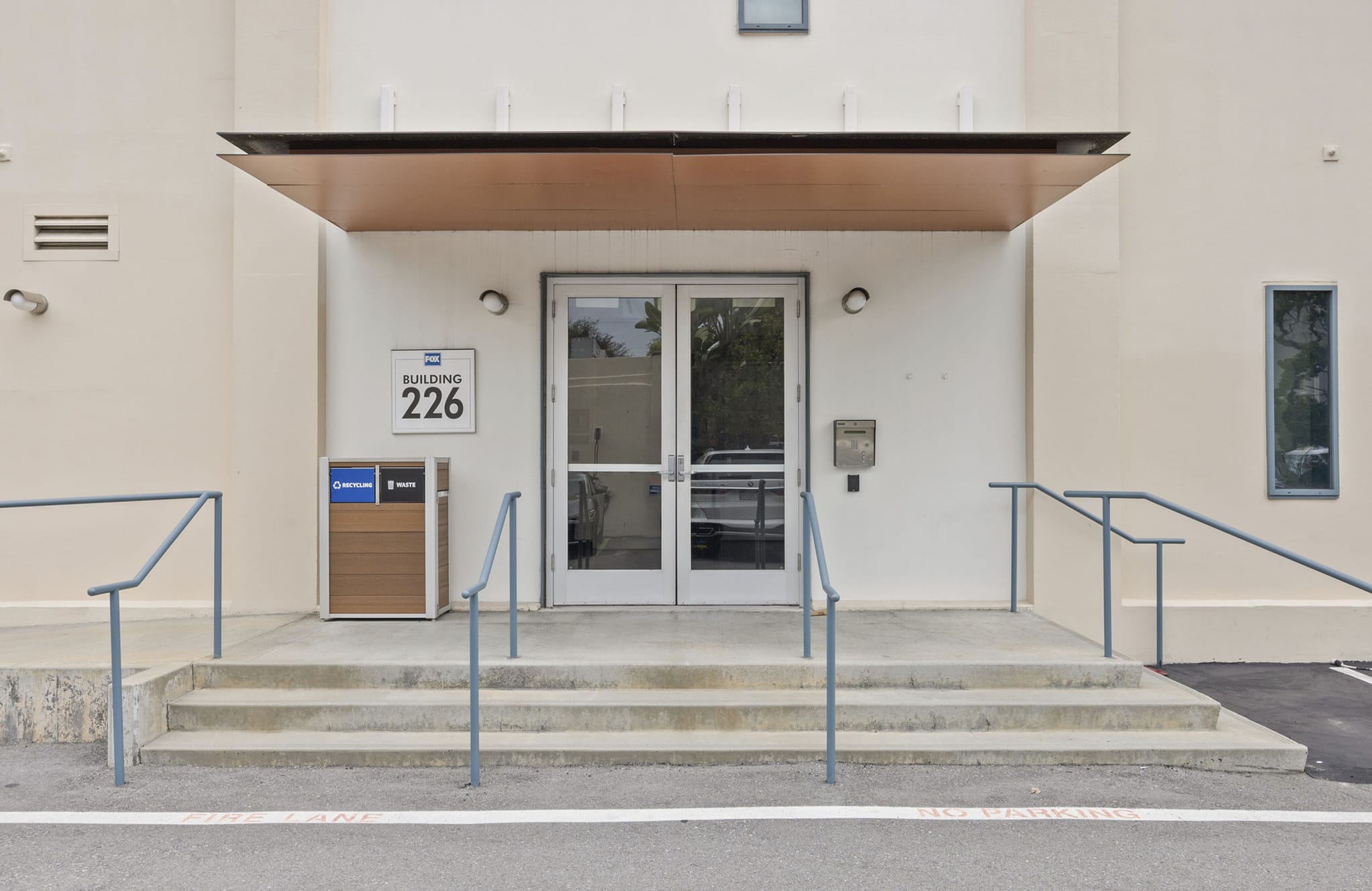 Building 226 entrance with glass doors, stairs, handrails, and a recycling bin.