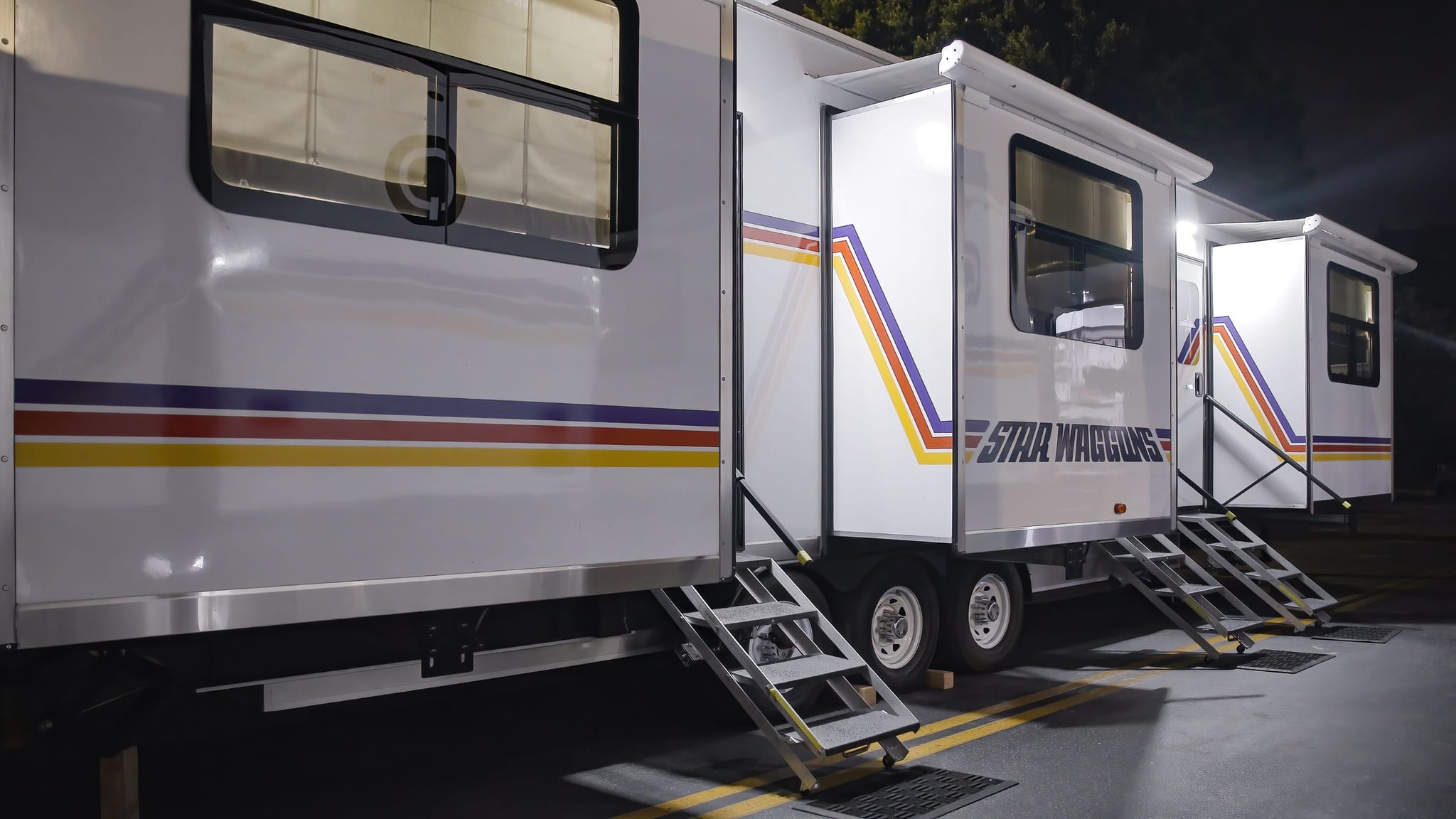 Star Waggons trailers with retro stripes and extended steps, illuminated at night.