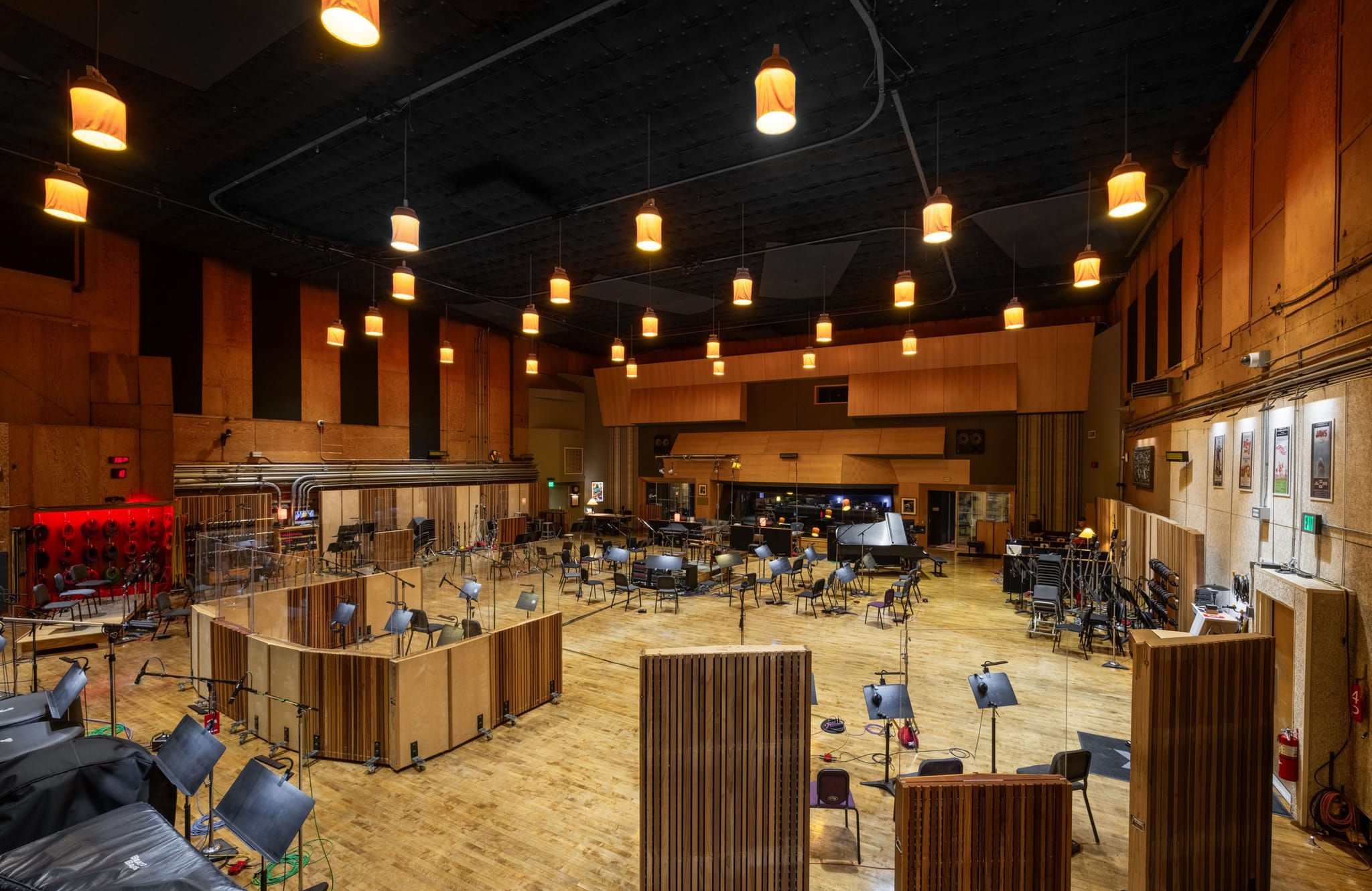 A large professional recording studio with numerous microphones, music stands, and wooden sound panels under warm lighting.