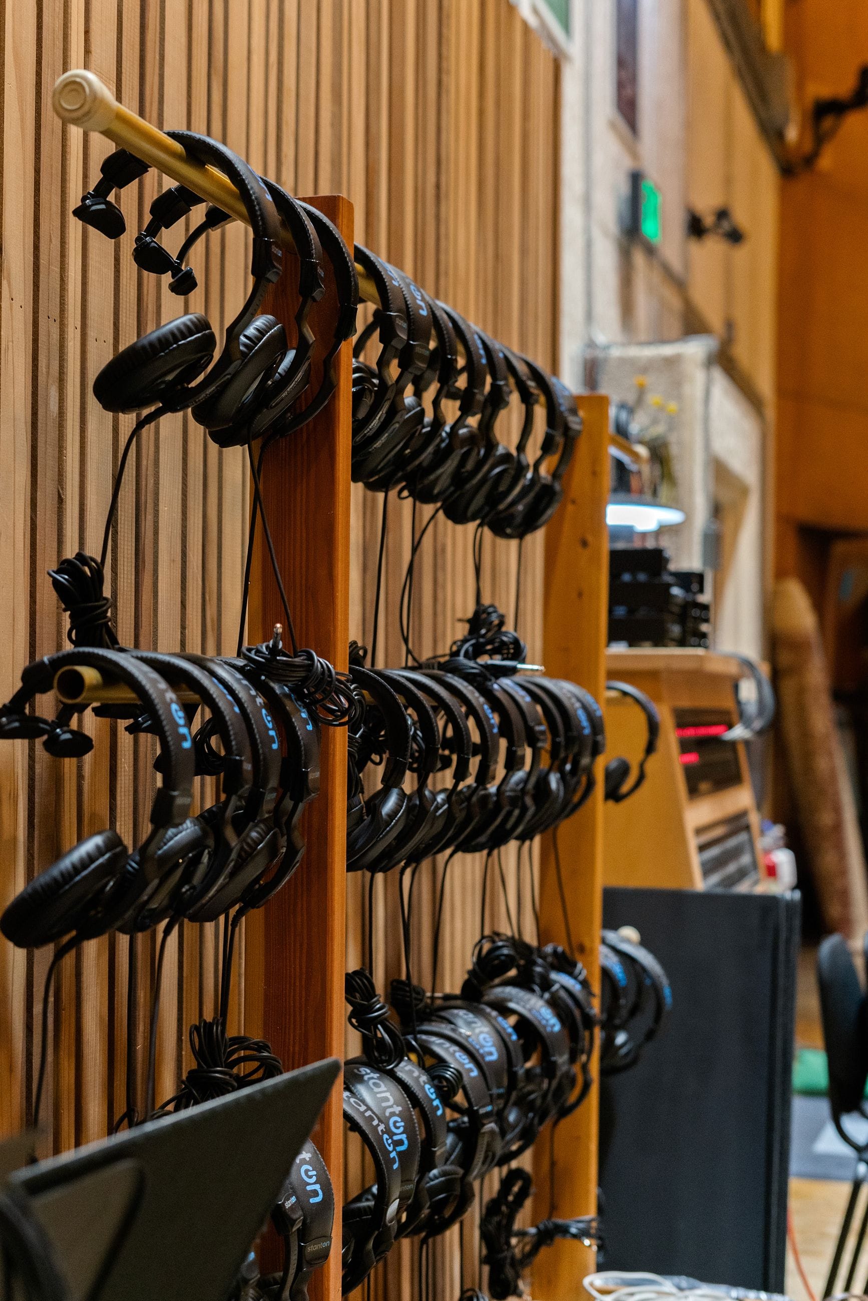 Rows of black headphones hanging on wooden racks against a wooden wall in a studio.