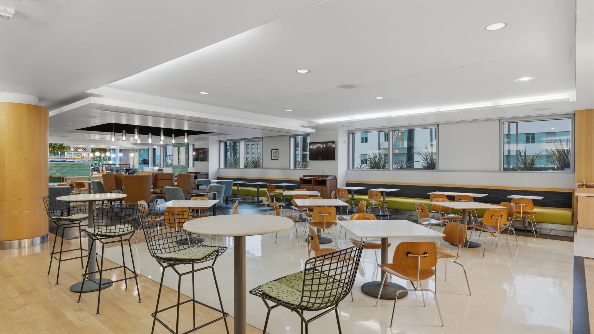 A bright, modern cafeteria space with various white-top tables, chairs, and bar stools.