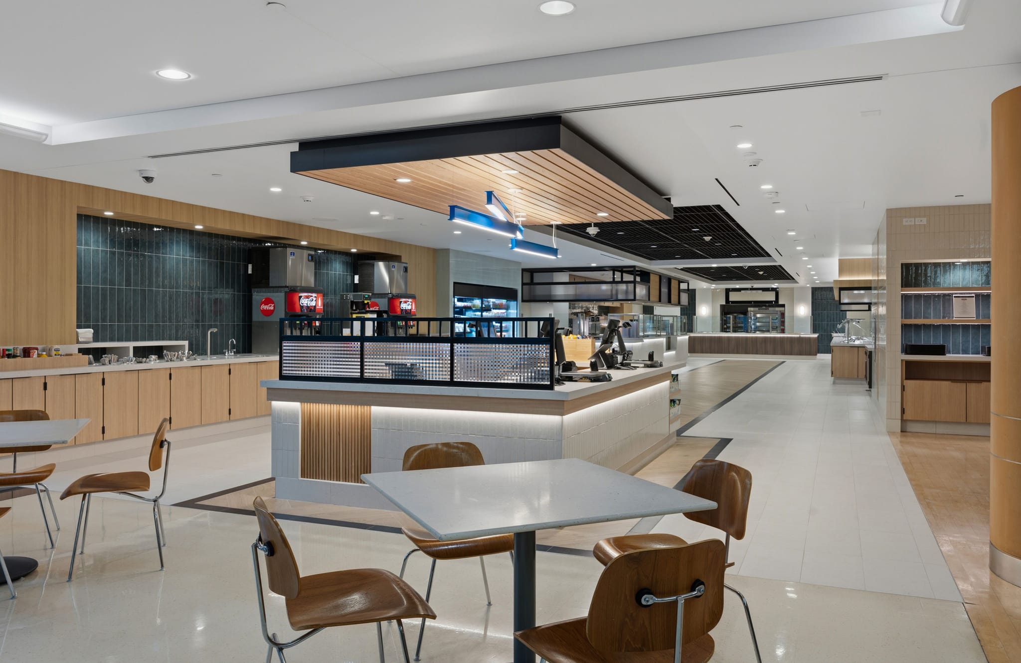 A modern, bright cafeteria with tables, chairs, and various food and drink serving stations.