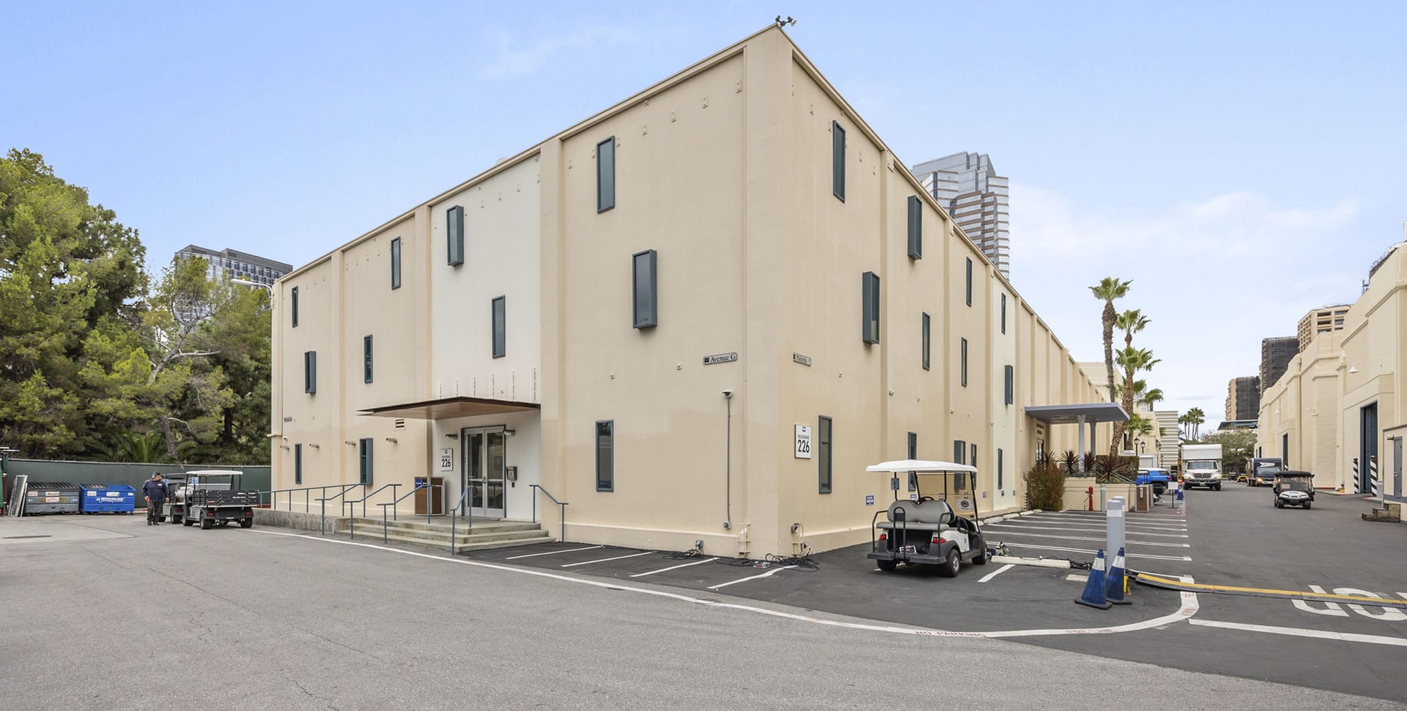 A large, light-colored studio building with a paved lot, several golf carts, and other vehicles parked outside.