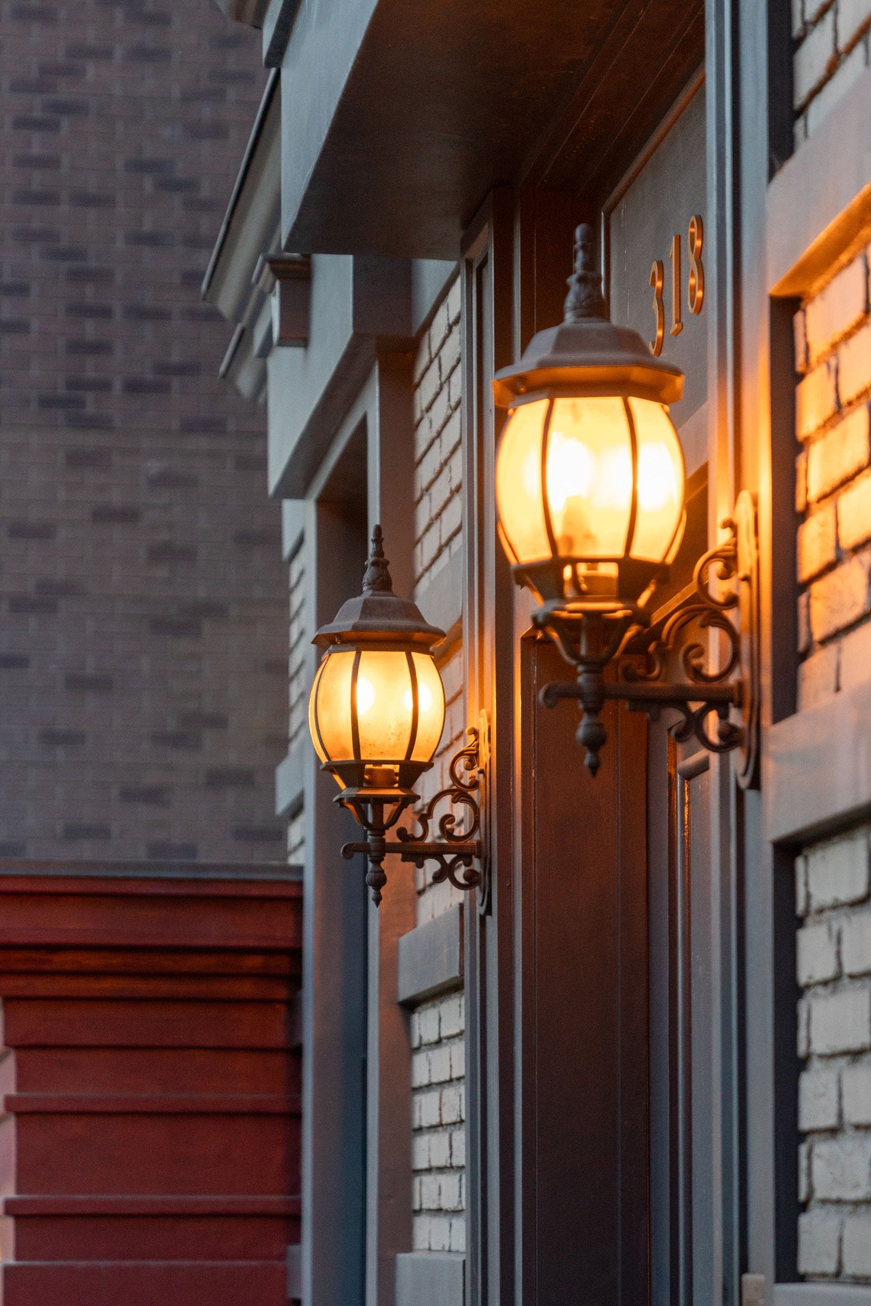 Two ornate, glowing outdoor lamps on a brick building with the number 318.