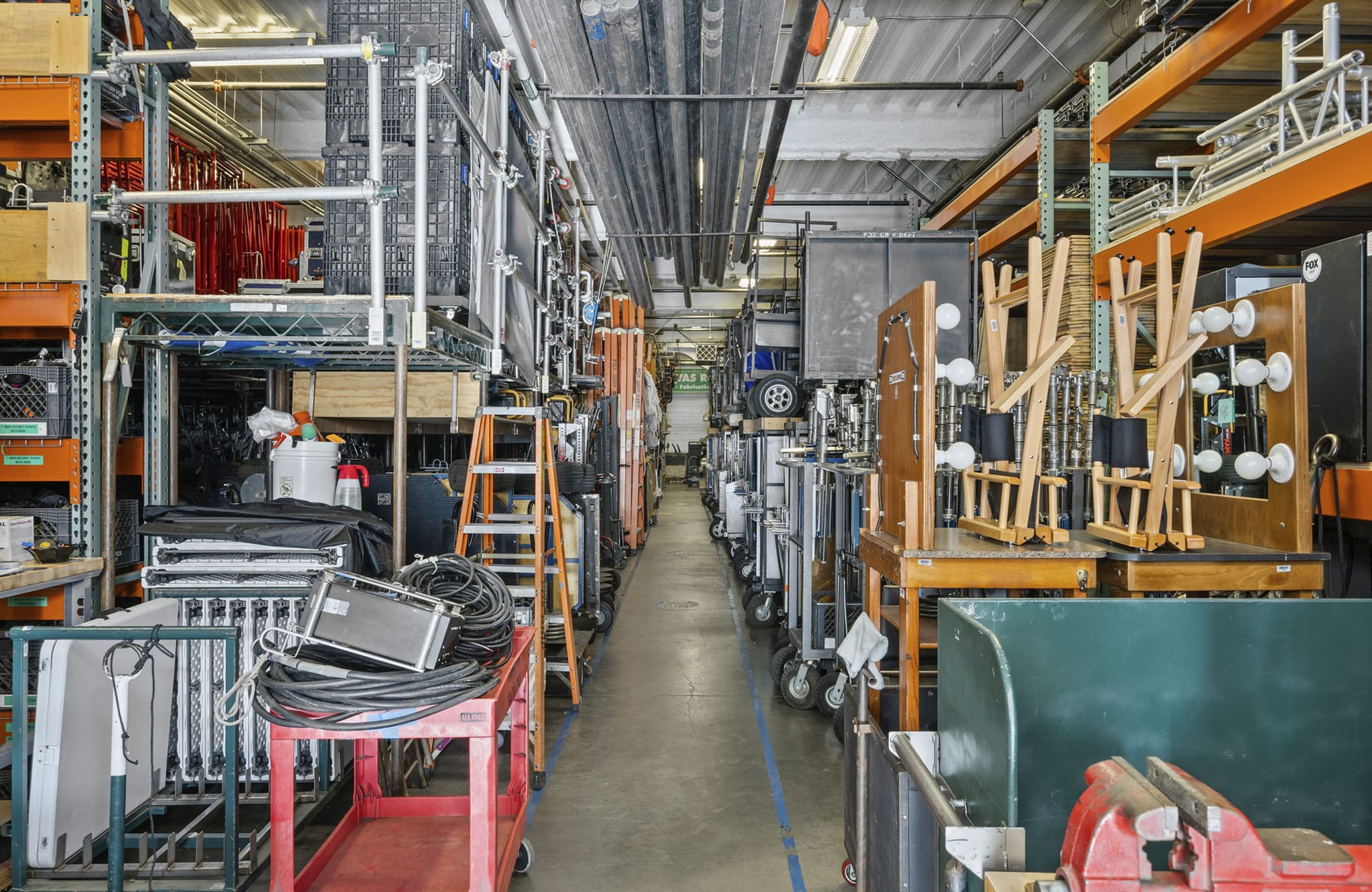 A long aisle in a warehouse filled with shelves, production equipment, and carts.