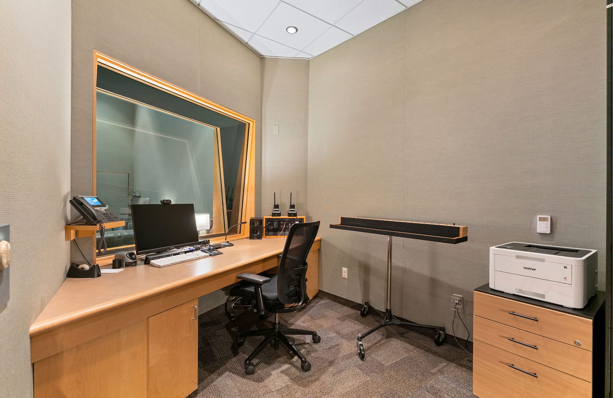A control room with a large observation window, a computer on a wooden desk, and a printer.