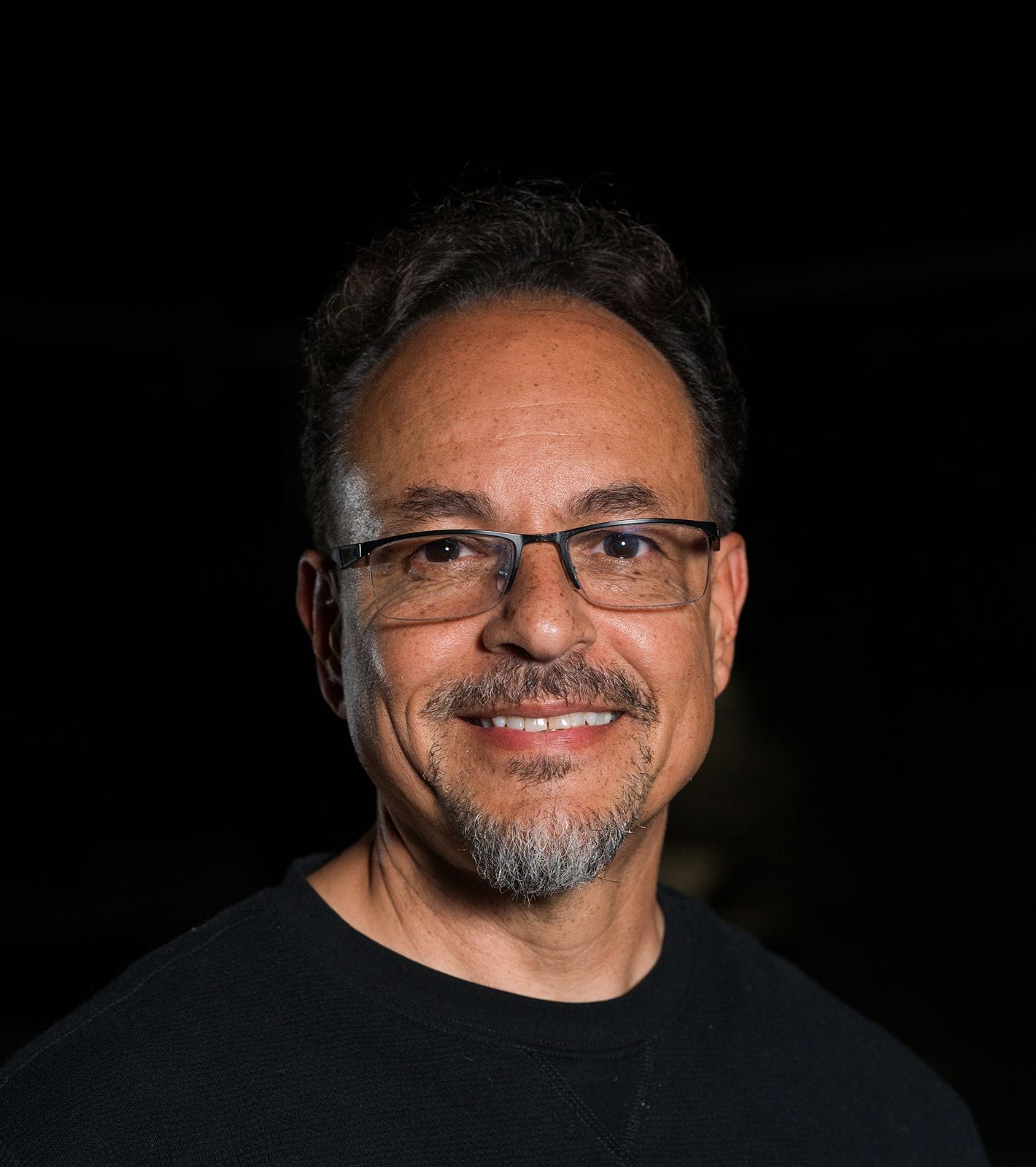 Smiling man with glasses and a goatee in a black shirt.