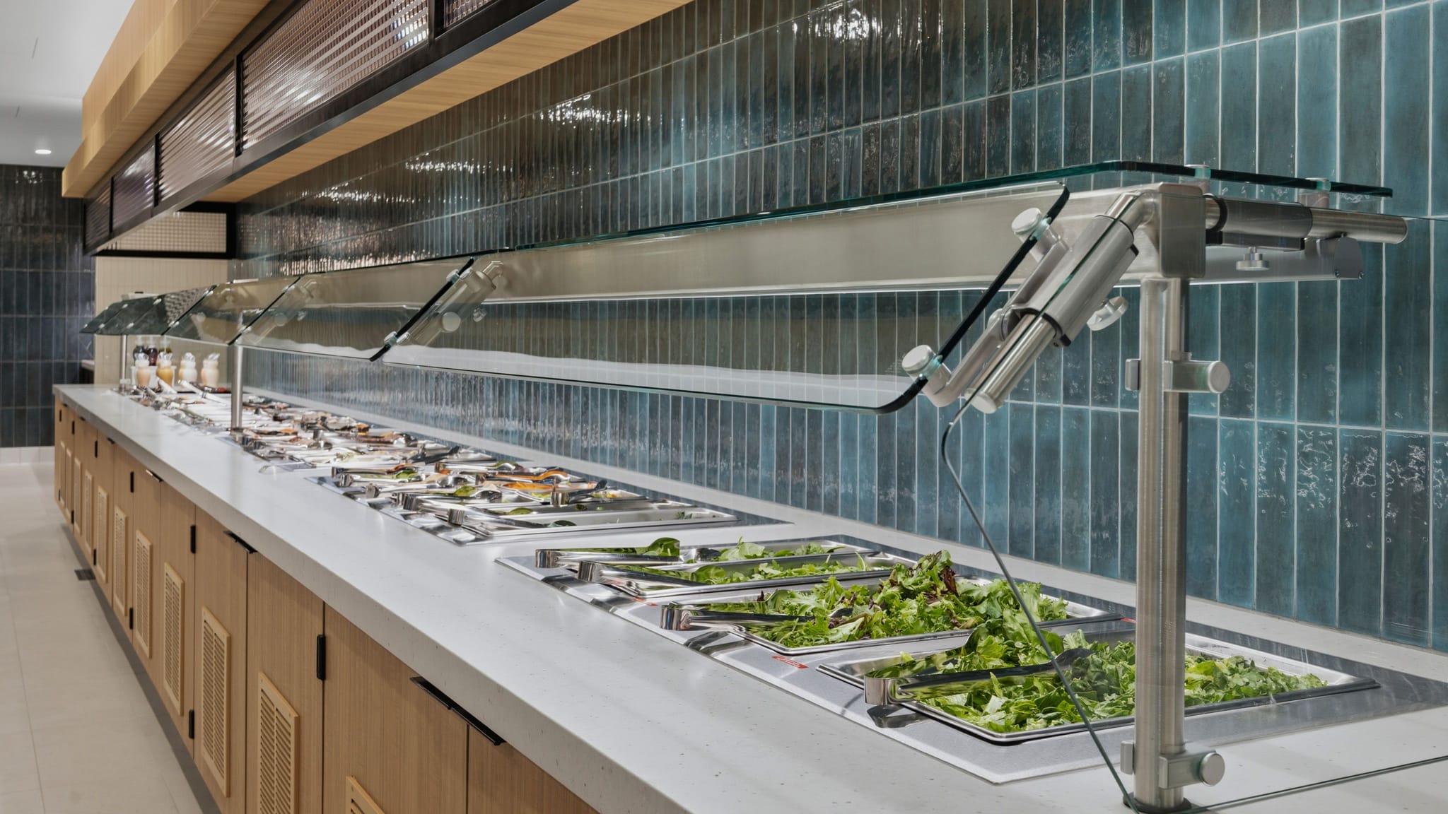 A modern self-service salad bar filled with fresh greens and toppings under glass sneeze guards.