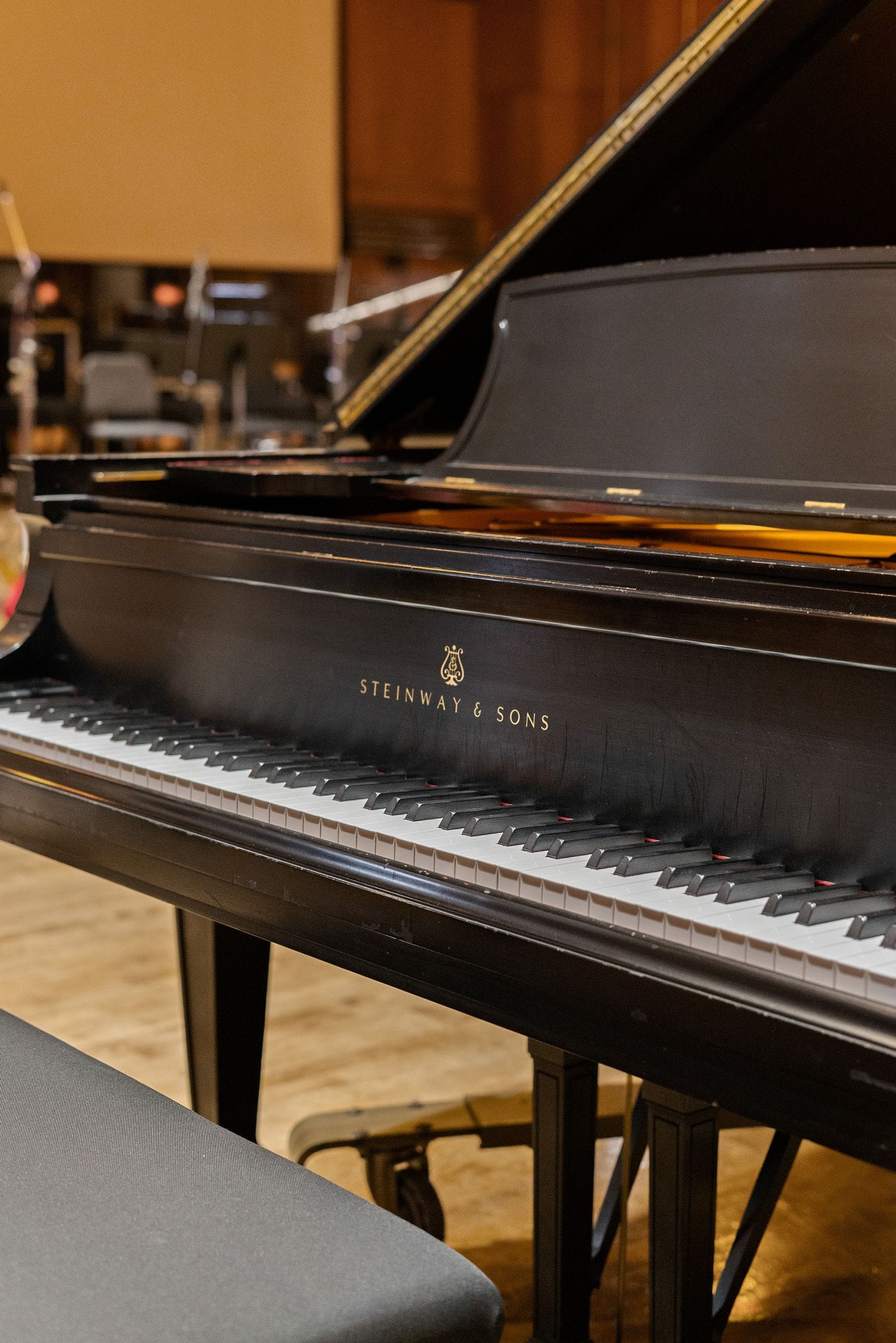 Black Steinway & Sons grand piano with its lid raised, showing the keys, and a bench in the foreground.