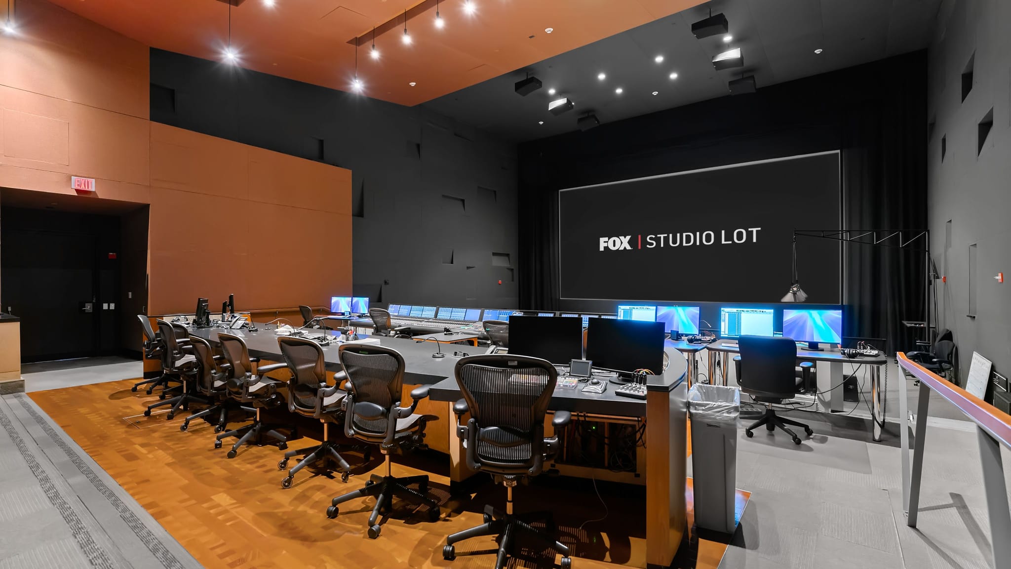 A modern control room with a long table, many computer monitors, and a large screen displaying "FOX | STUDIO LOT."