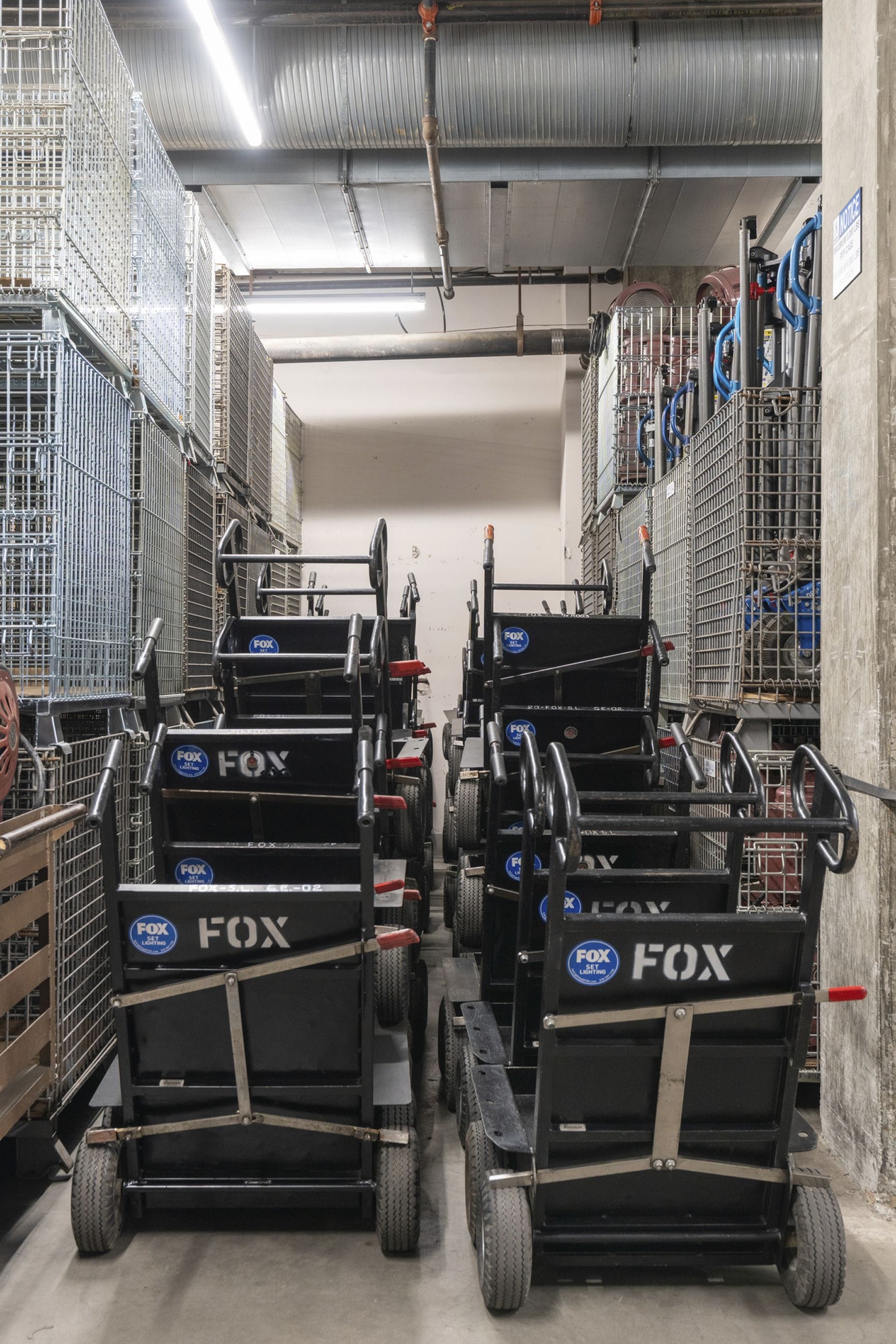 Rows of black FOX utility carts in a storage hallway lined with metal shelving.