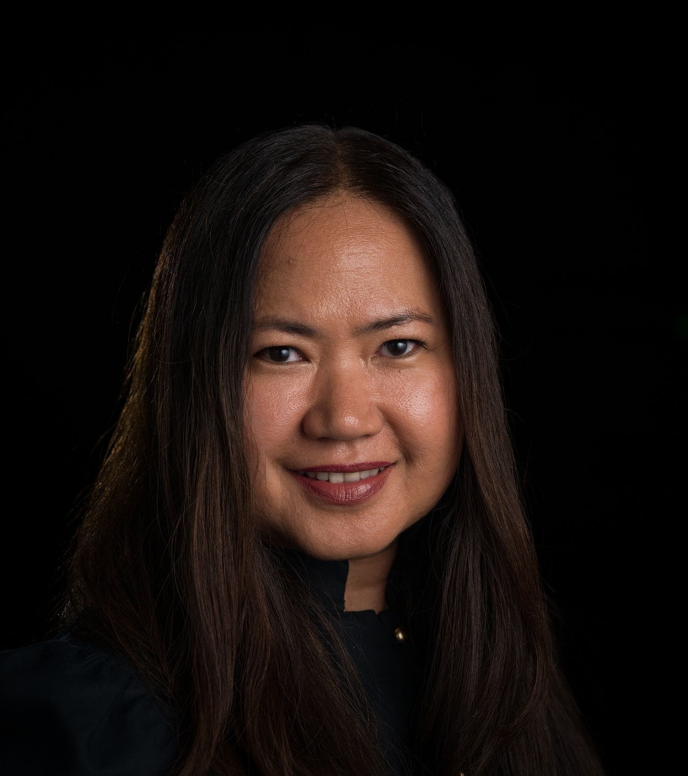 A smiling woman with long dark hair against a black background.