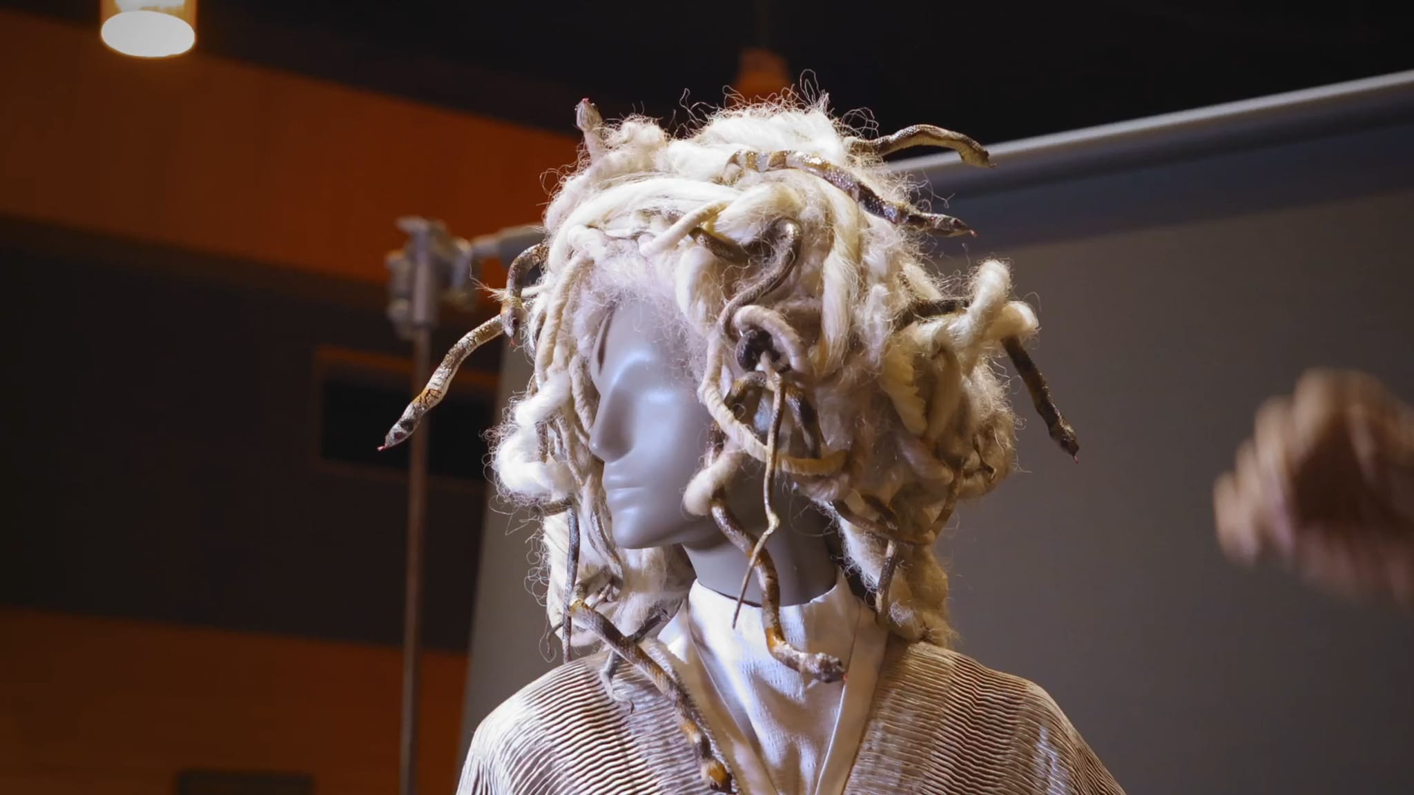 Mannequin in profile wearing an elaborate wig of light dreadlocks and dark snake-like strands.