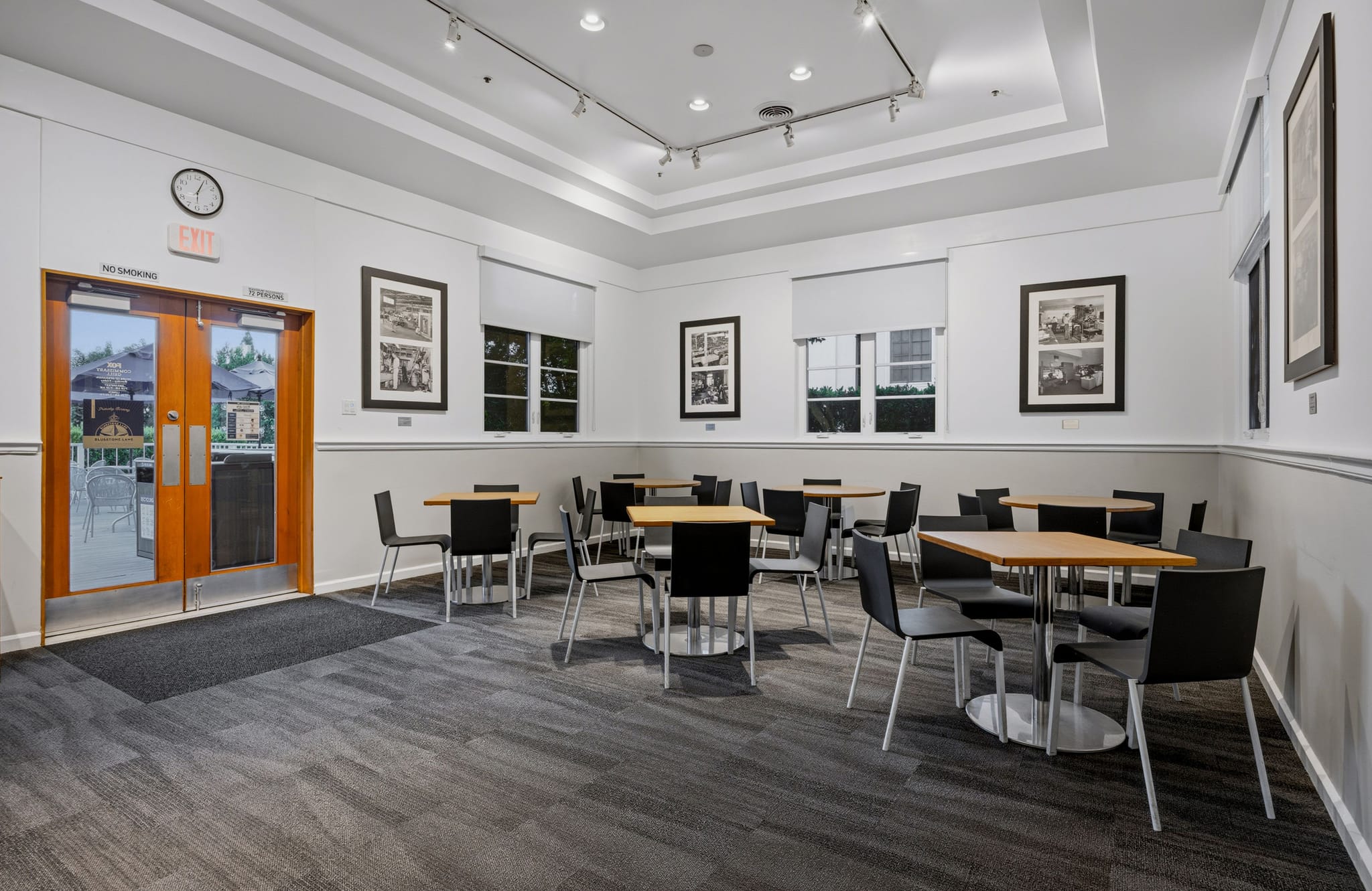 A bright, modern cafe or lounge area with multiple tables and chairs, artwork on the walls, and an exit leading outside.