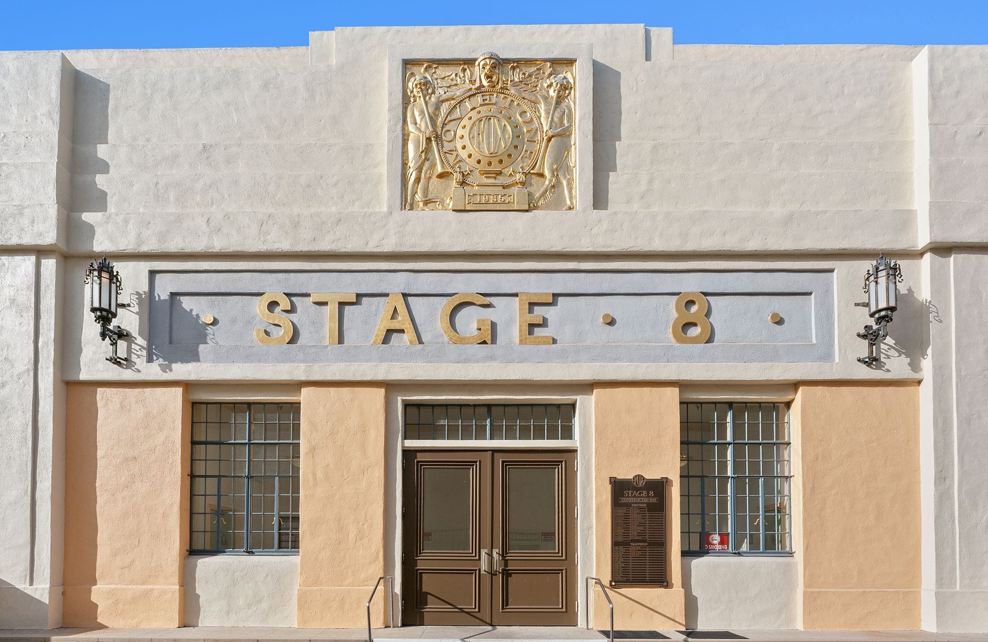 Cream and peach Art Deco building with "STAGE 8" in gold letters, a golden relief, and double doors.