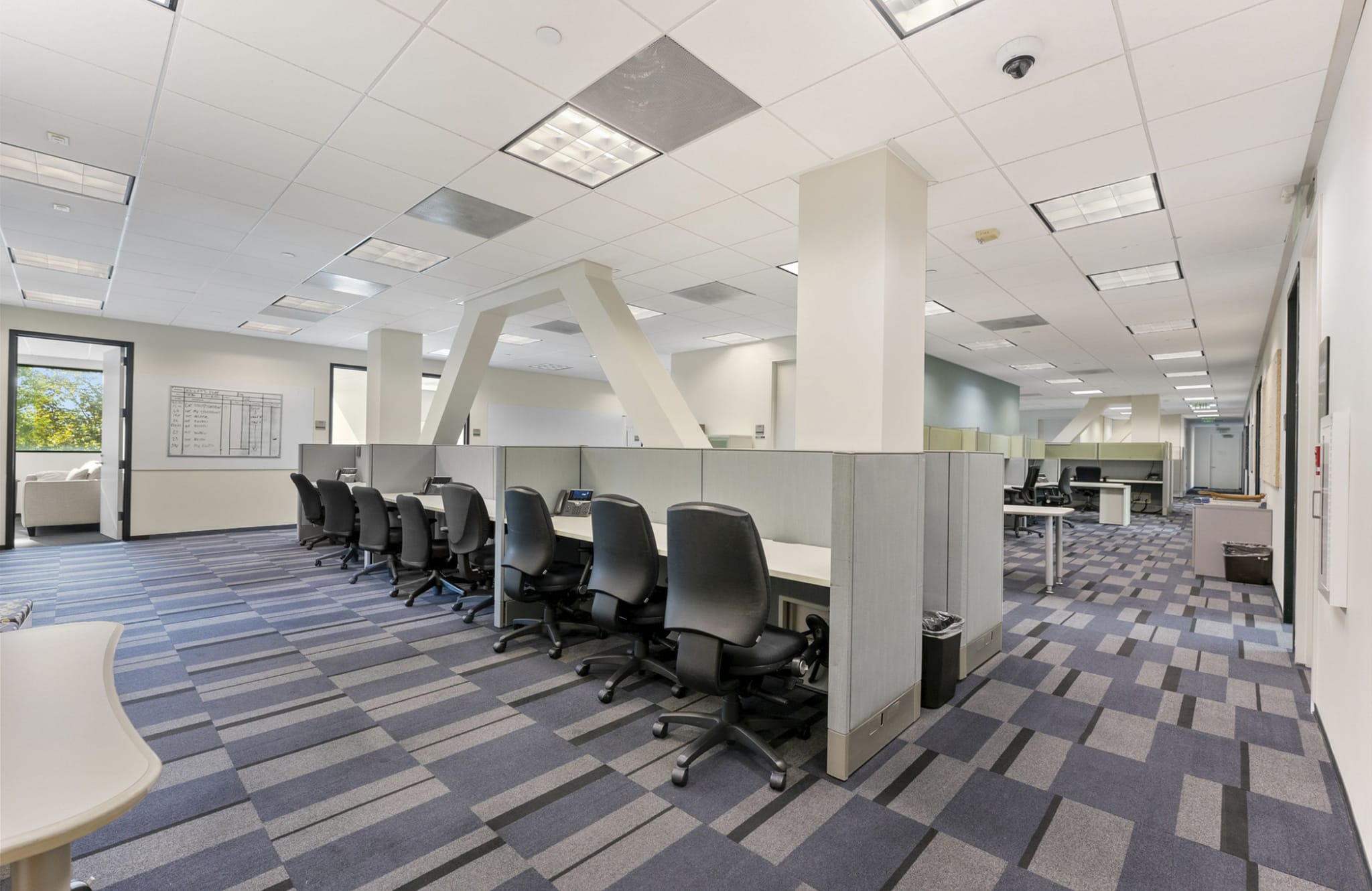 An empty office space with rows of cubicles, office chairs, and a blue and grey patterned carpet.