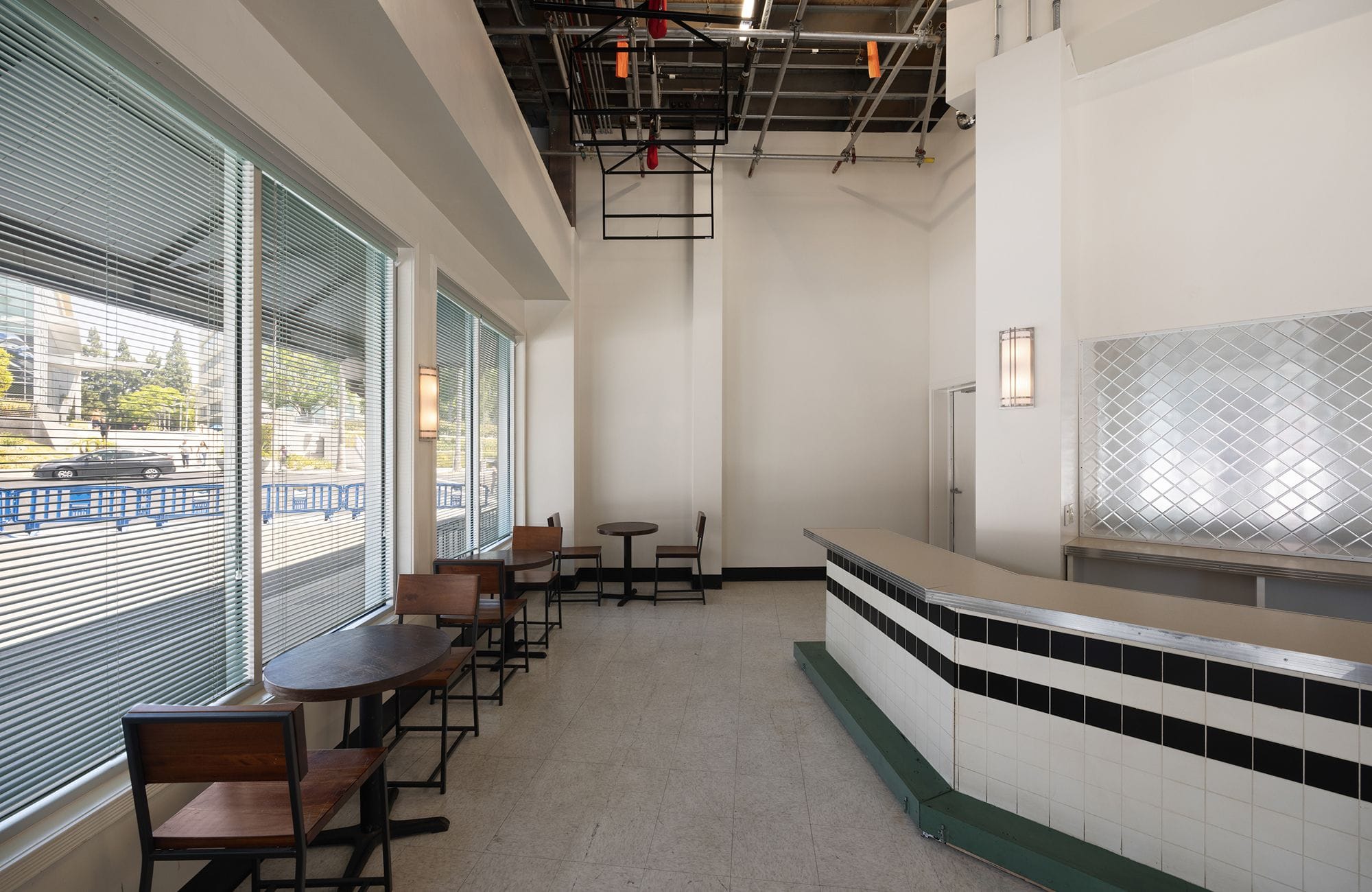 Empty diner or cafe interior with windows, tables, and a black and white tiled counter.