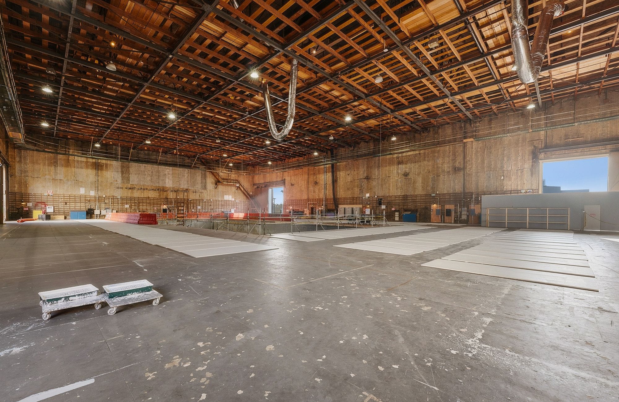 Spacious empty industrial warehouse with a high wooden ceiling, concrete floor, and some white panels laid out.