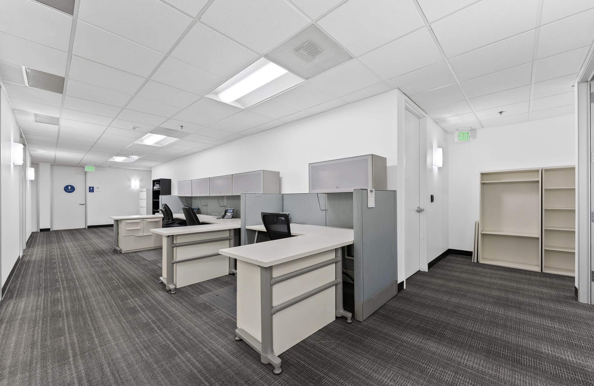 An empty modern office with grey cubicles, black chairs, patterned grey carpet, and white walls.