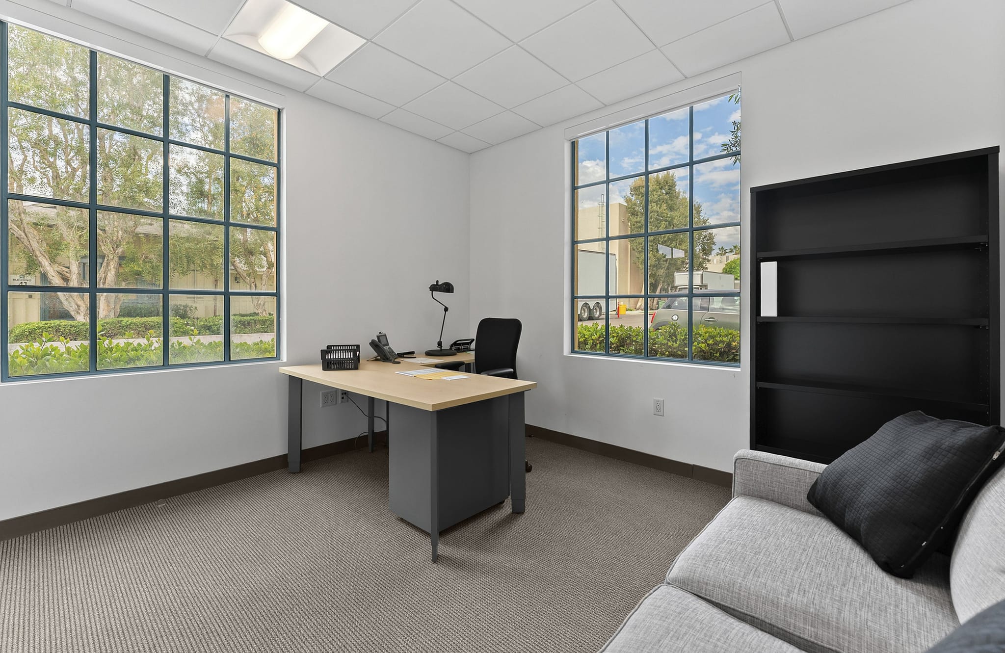 Bright office with grid windows, a desk, chair, bookshelf, and couch.