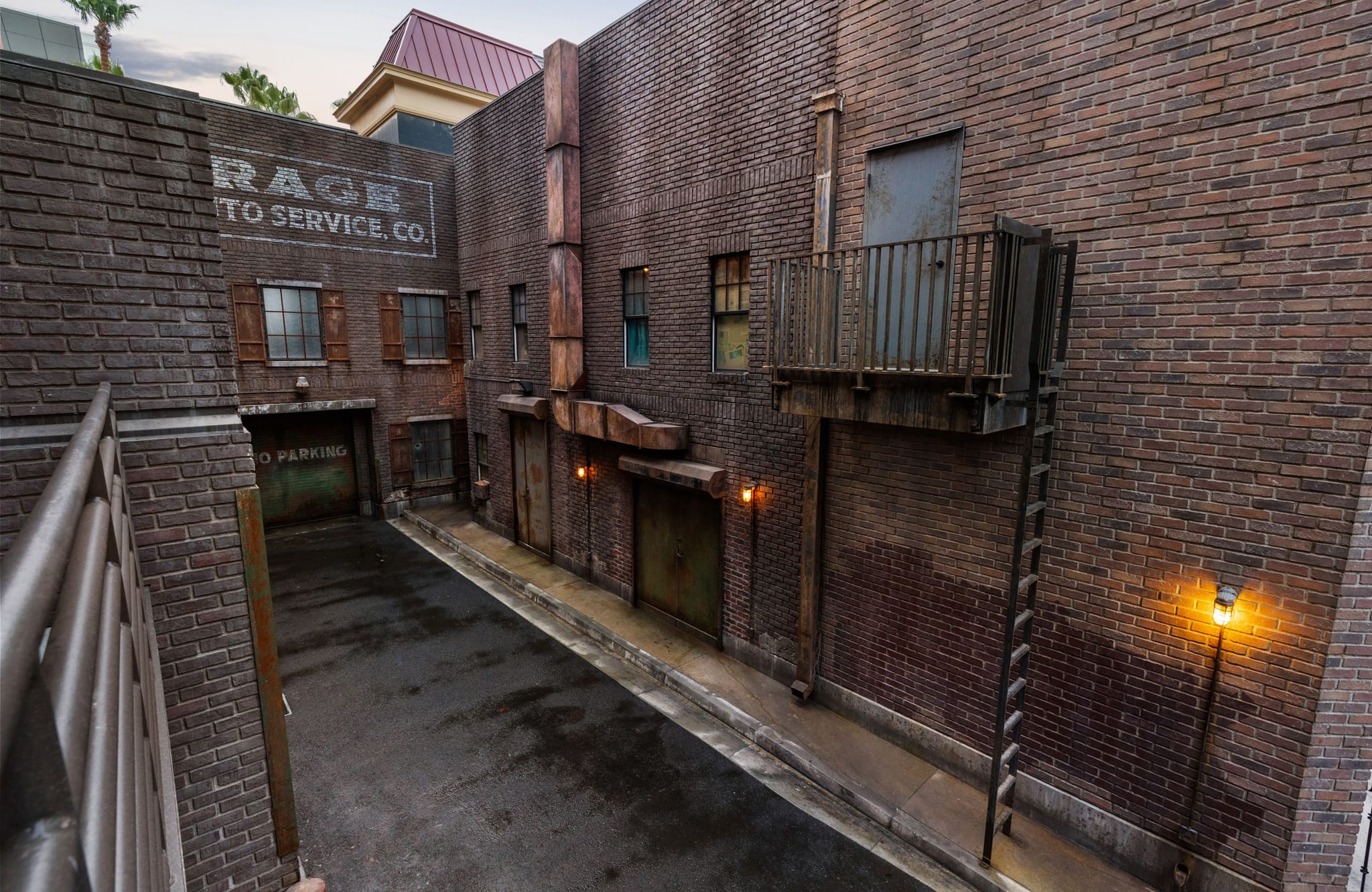 A brick urban alleyway with a "RAGE AUTO SERVICE, CO." sign, a metal balcony, and lit street lamps.