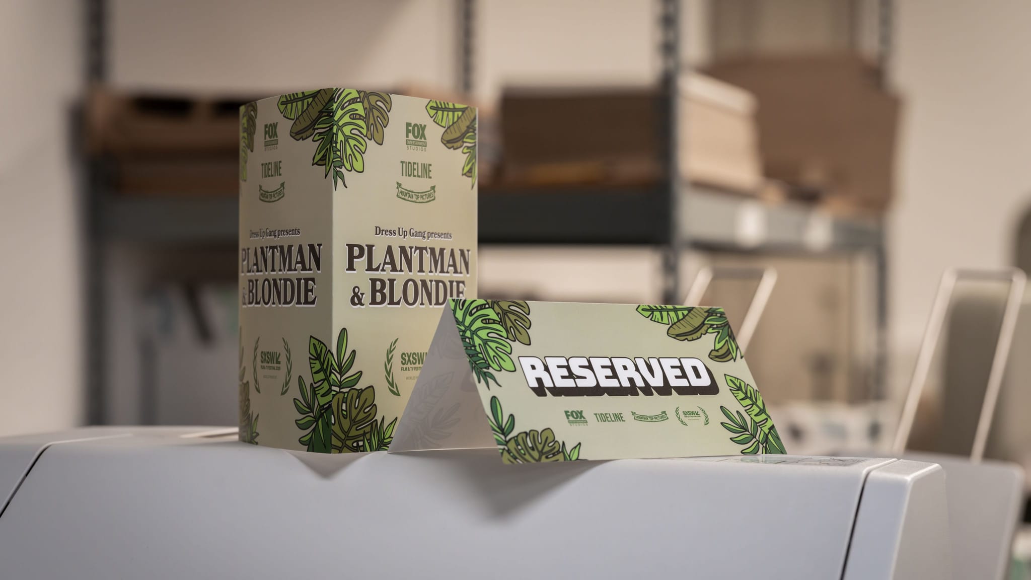 Packaging for "Plantman & Blondie" and a "Reserved" tent card, both featuring a green leaf design, sit on a white surface.