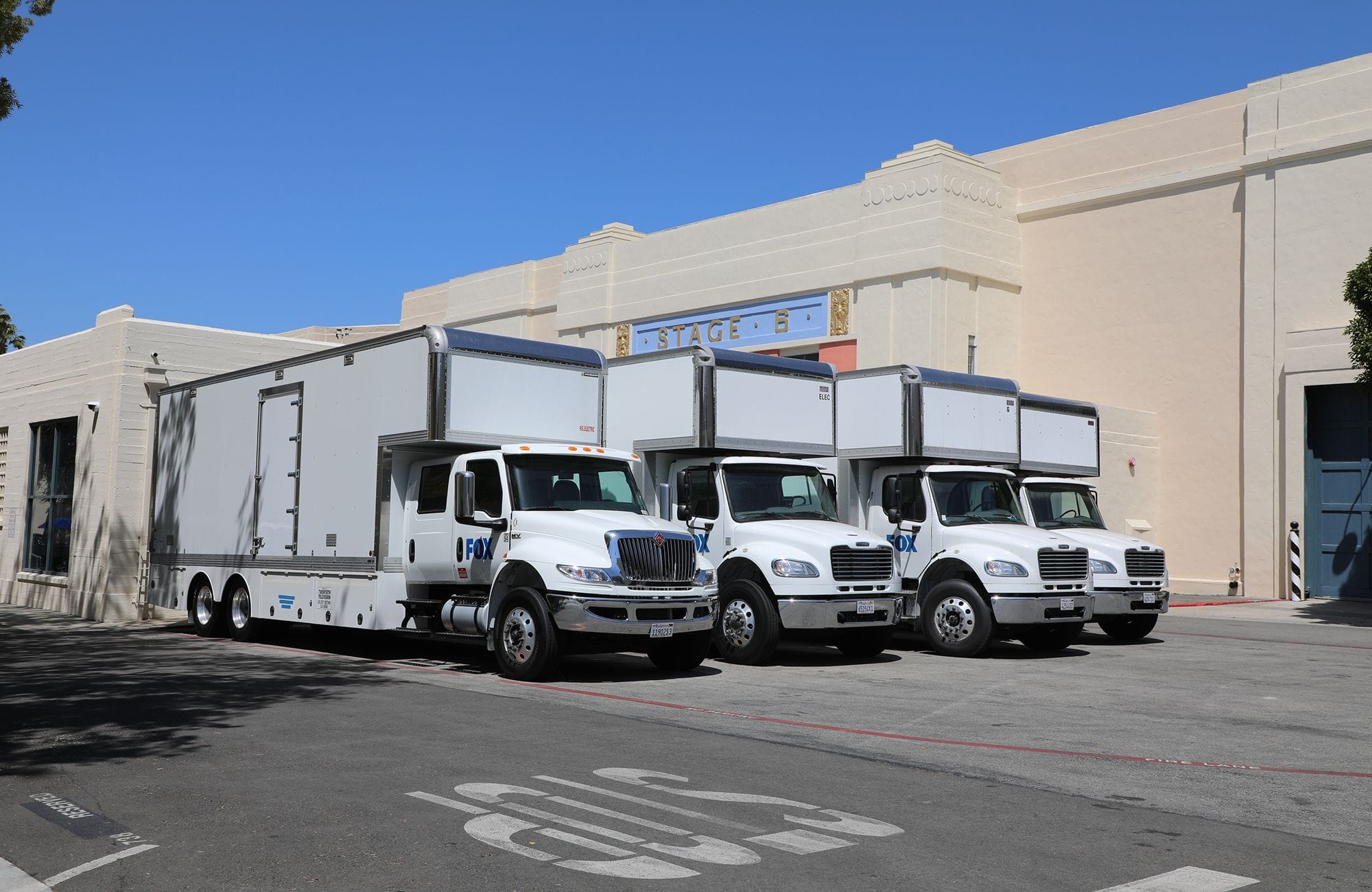 Four white FOX production trucks parked in front of Stage B.
