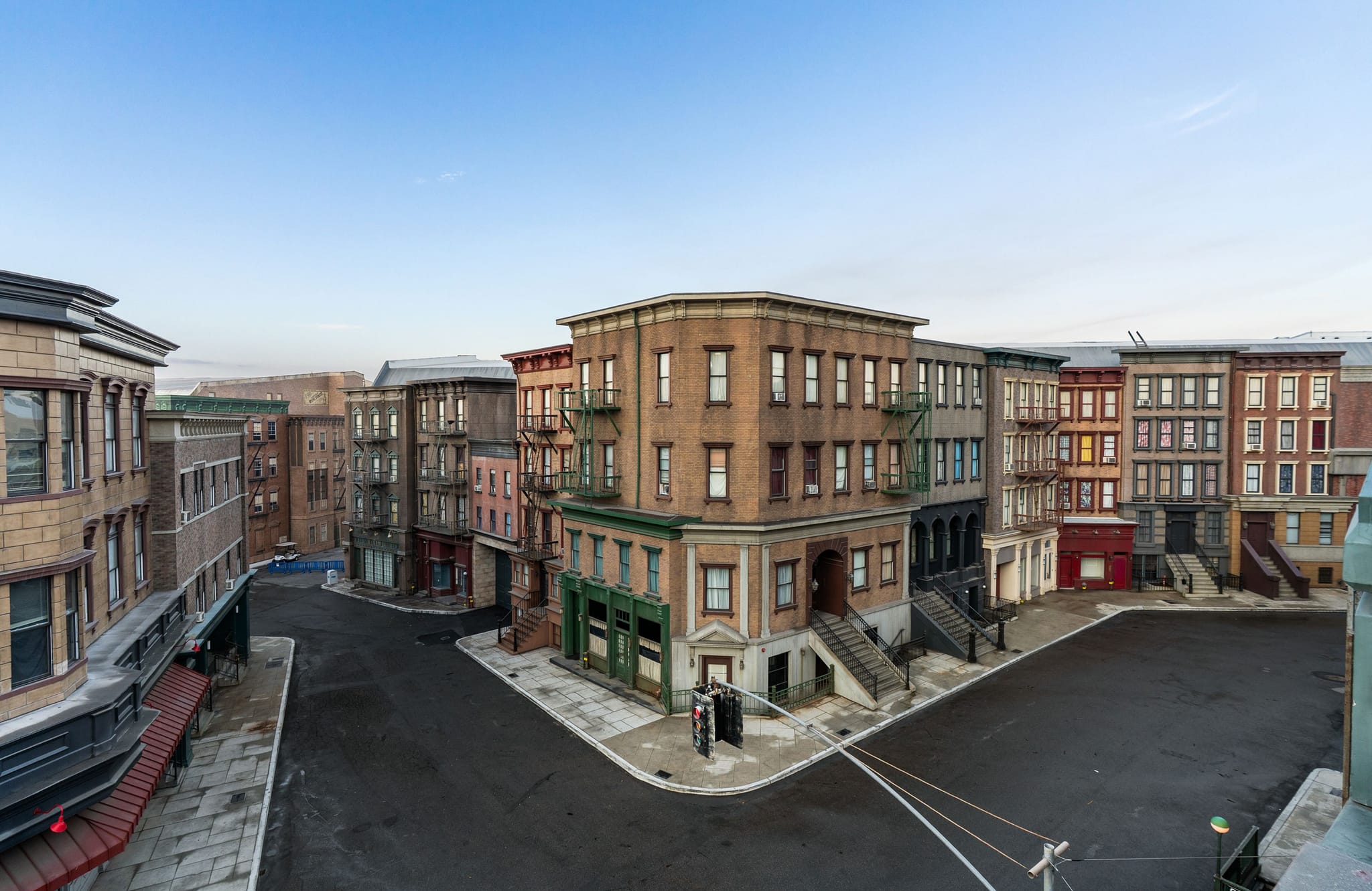 An empty urban street with multi-story buildings, many featuring fire escapes, under a clear blue sky.