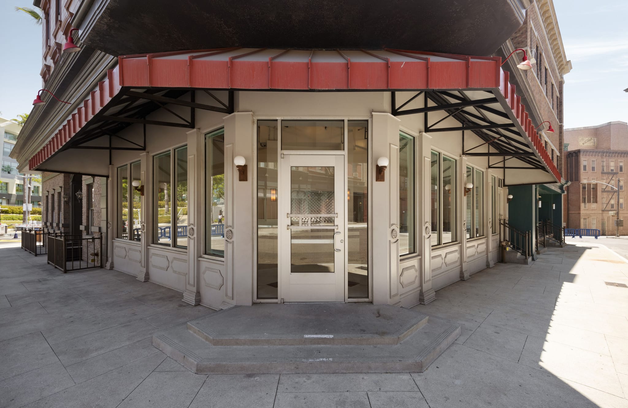 A vacant corner shop with large windows, a glass door, and a red awning.