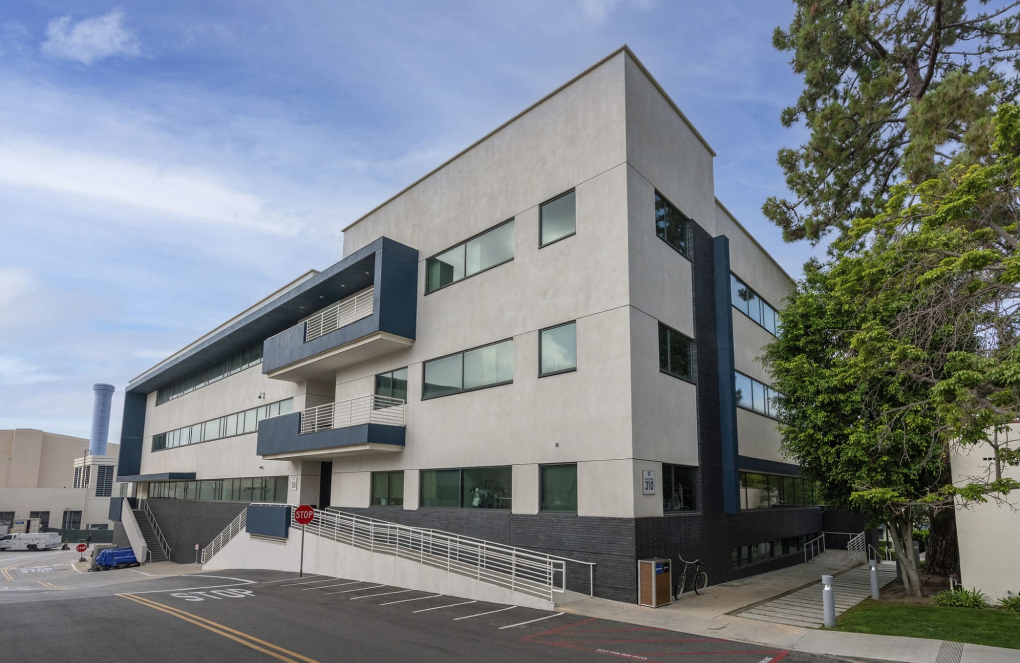 A modern three-story building with light walls, dark blue accents, and a long accessible ramp leading to its entrance.