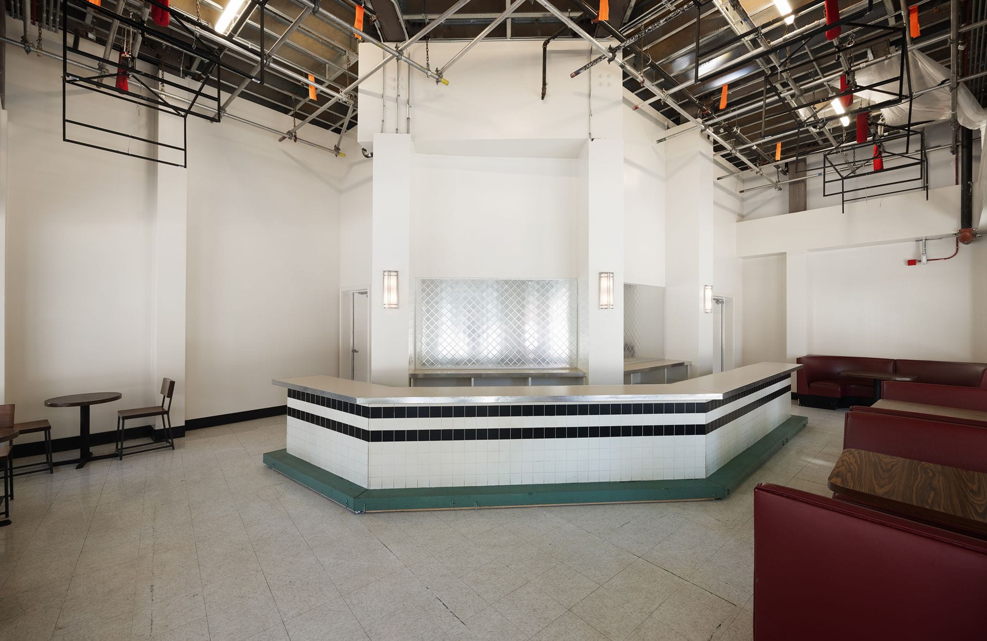 An empty diner with a black and white tiled counter, red booths, and an exposed ceiling.